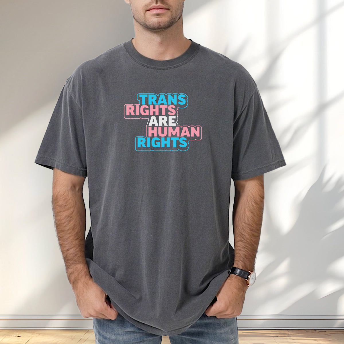 Male model wearing pepper t-shirt with graphic reading "trans rights are human rights" in the colors of the trans flag.