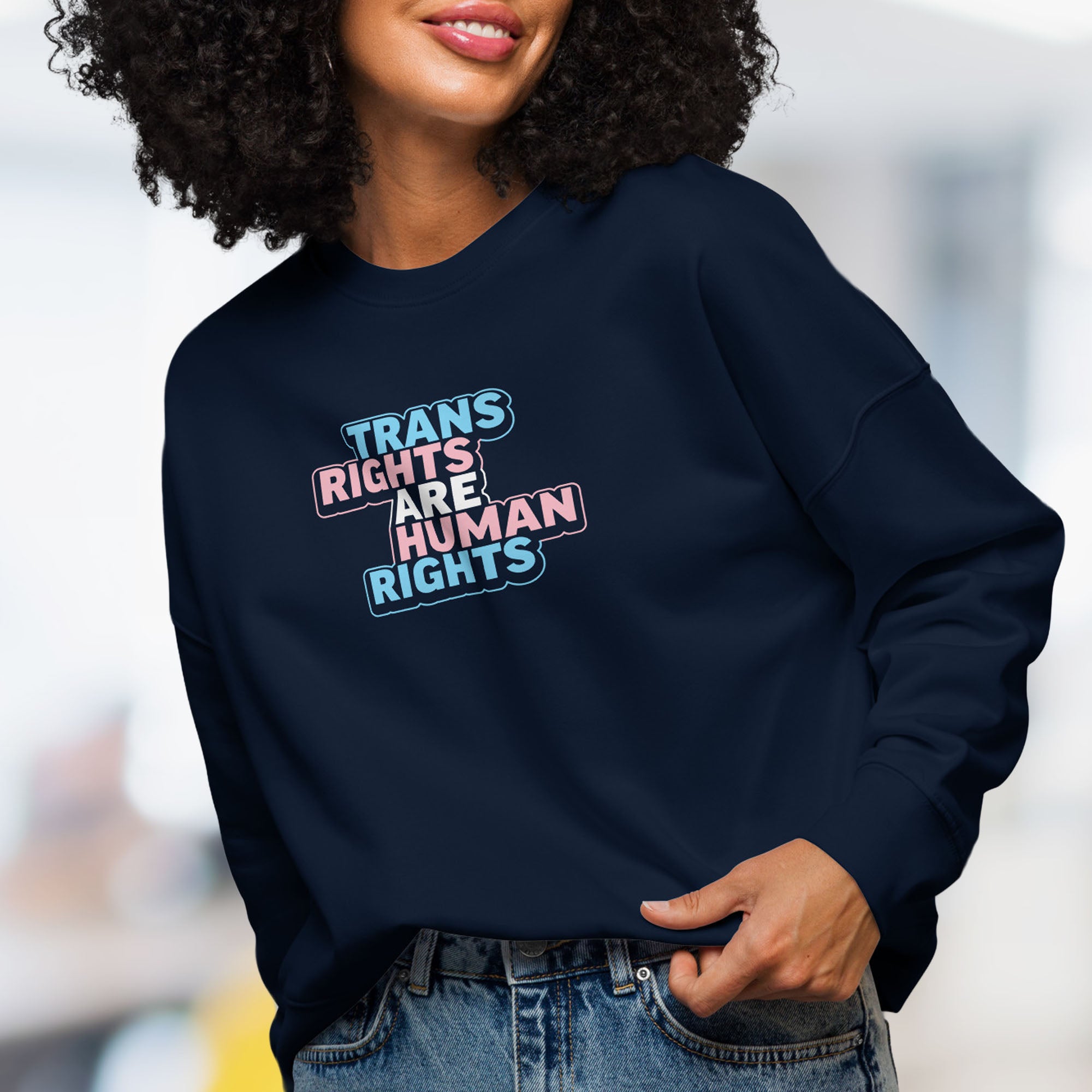 Female model wearing navy women's crewneck sweatshirt with graphic that reads "trans rights are human rights" in the light blue, pink, and white colors of the trans flag.