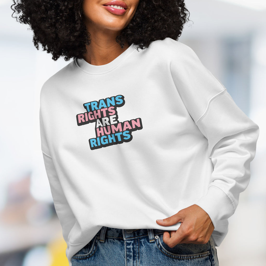 Female model wearing white women's crewneck sweatshirt with graphic that reads "trans rights are human rights" in the light blue, pink, and white colors of the trans flag.