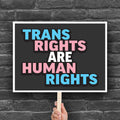 Protest sign that reads “Trans Rights Are Human Rights” in blue, pink, and white lettering, symbolizing support for transgender equality and resistance to discrimination under the Trump administration.