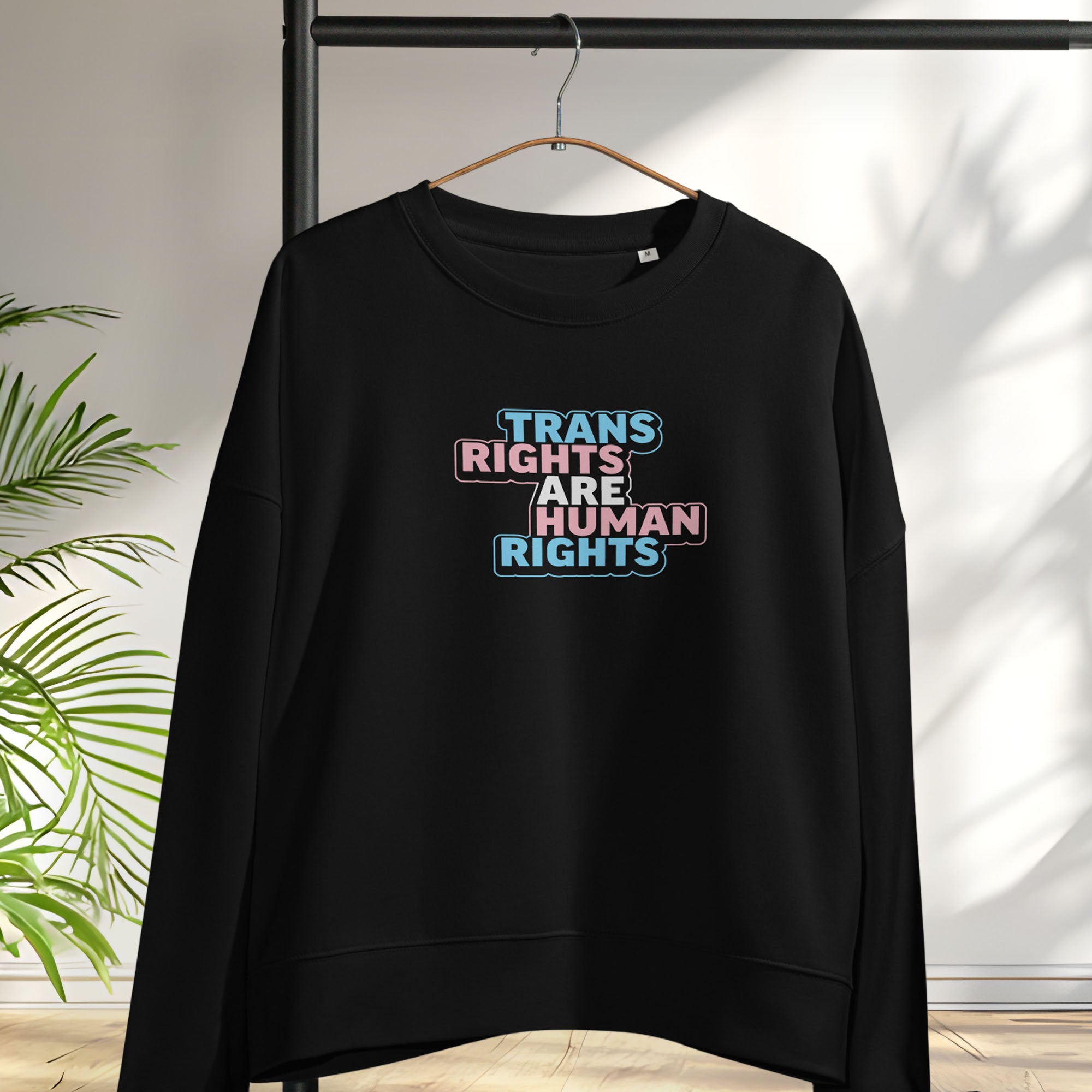 Hanging black women's crewneck sweatshirt with graphic that reads "trans rights are human rights" in the light blue, pink, and white colors of the trans flag.