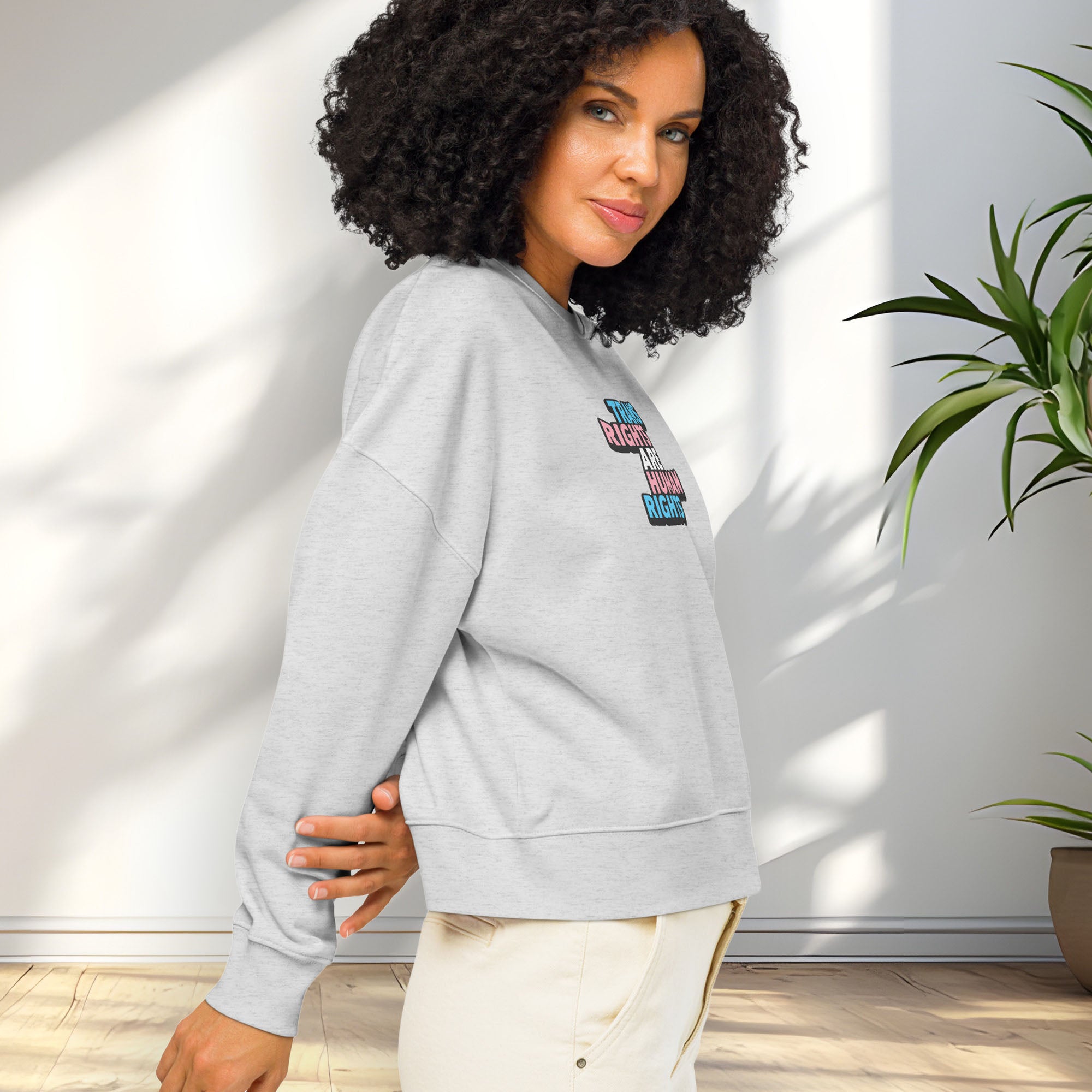 Side view of female model wearing grey women's crewneck sweatshirt with graphic that reads "trans rights are human rights" in the light blue, pink, and white colors of the trans flag, showing shirt fit.