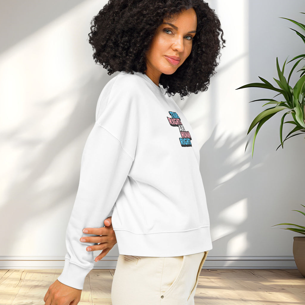 Side view of female model wearing white women's crewneck sweatshirt with graphic that reads "trans rights are human rights" in the light blue, pink, and white colors of the trans flag, showing shirt fit.
