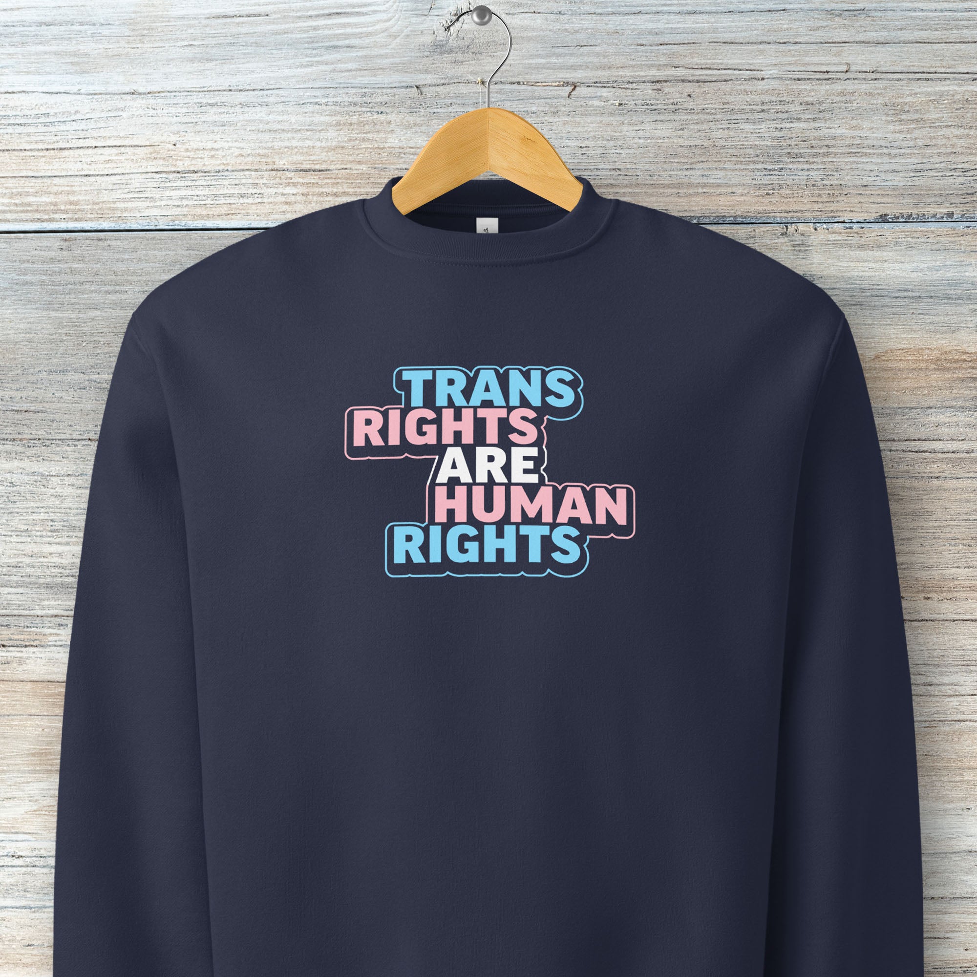 Navy crewneck sweatshirt with graphic that reads "trans rights are human rights" in the light blue, pink, and white colors of the trans flag, with a colorful outline around the text block.