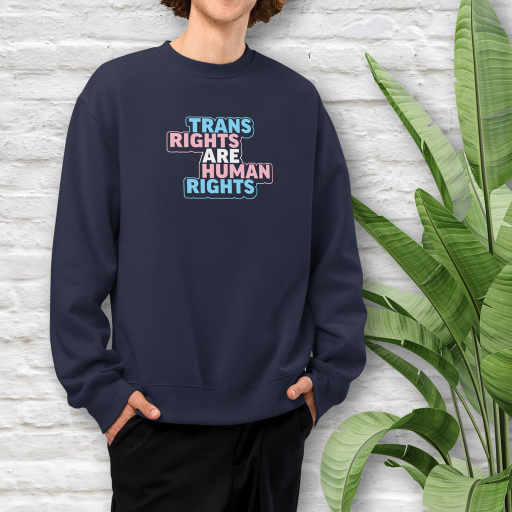 Male model wearing navy crewneck sweatshirt with graphic that reads "trans rights are human rights" in the light blue, pink, and white colors of the trans flag, with a colorful outline around the text block.