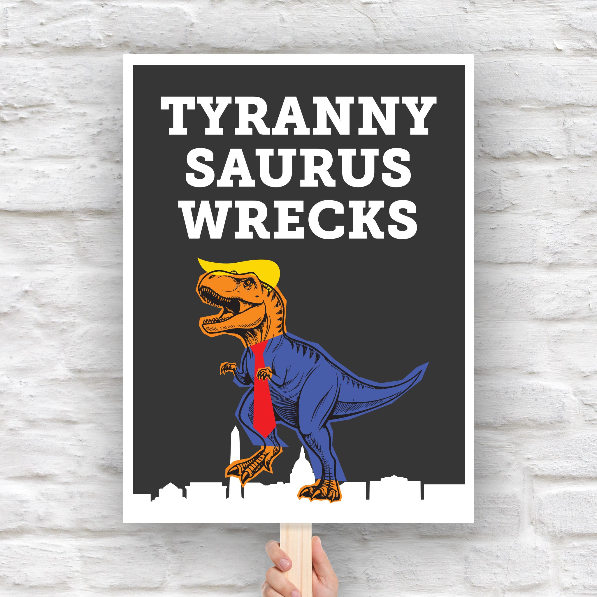 Funny anti-trump protest sign featuring a line drawing of a t-rex tyrannosaurus rex dinosaur with orange skin, wearing a blue suit, red tie, and yellow hair resembling Donald Trump, with the caption “TYRANNY SAURUS WRECKS” in bold white letters above. The dinosaur is stepping on a silhouette of the Washington D.C. skyline.