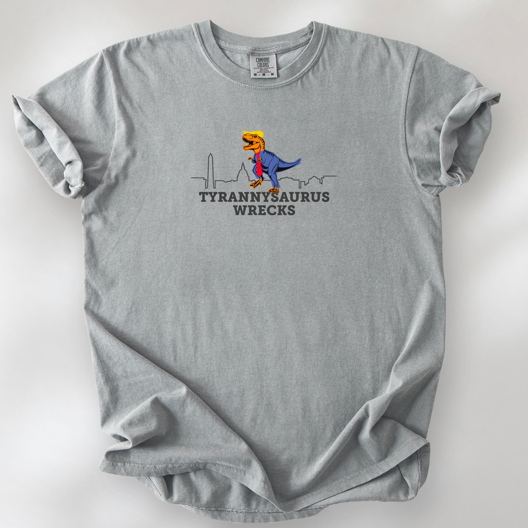 Granite t-shirt with a funny drawing of an orange t-rex dinosaur dressed in a blue suit with a red tie that's too long, stupid yellow hair, and tiny hands. The dinosaur is stepping on a line drawing of the Washington DC skyline. Under the dinosaur is bold text that reads "tyranny saurus wrecks."
