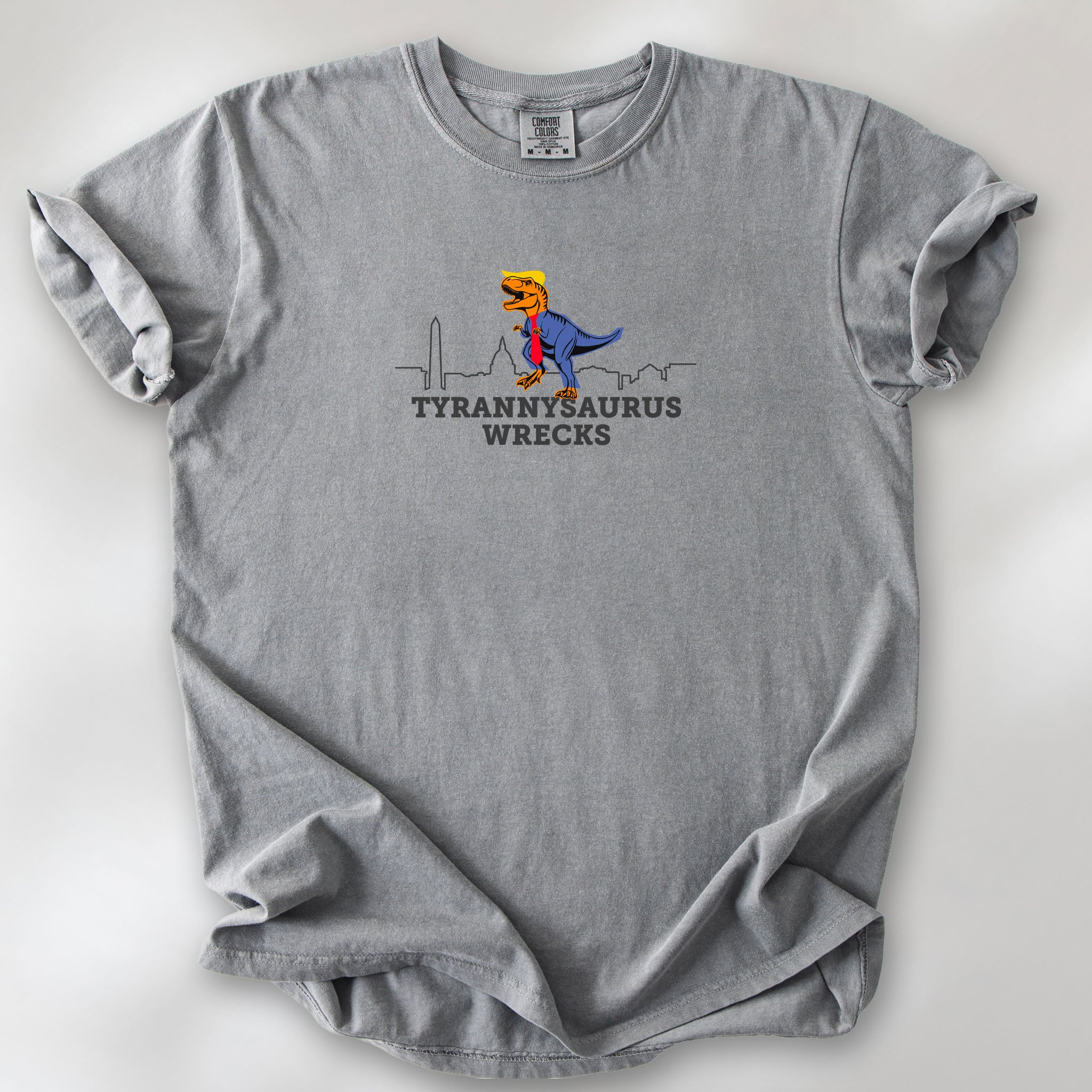 Grey t-shirt with a funny drawing of an orange t-rex dinosaur. Includes size and fit information for the model who is 6 feet 0 inches, 176 pounds, and wearing a size XL shirt. T-Rex is dressed in a blue suit with a red tie that's too long, stupid yellow hair, and tiny hands. The dinosaur is stepping on a line drawing of the Washington DC skyline. Under the dinosaur is bold text that reads "tyranny saurus wrecks."