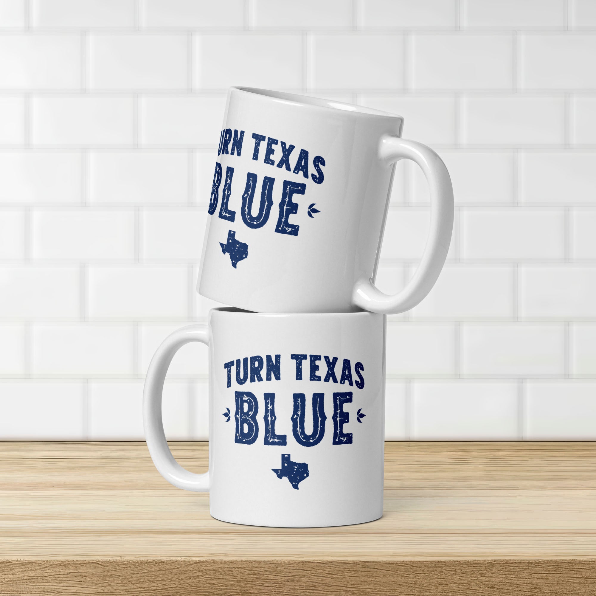 Two white ceramic coffee mugs featuring a distressed blue "Turn Texas Blue" design with a Texas state silhouette, stacked on a kitchen counter, showing the same design on each side.