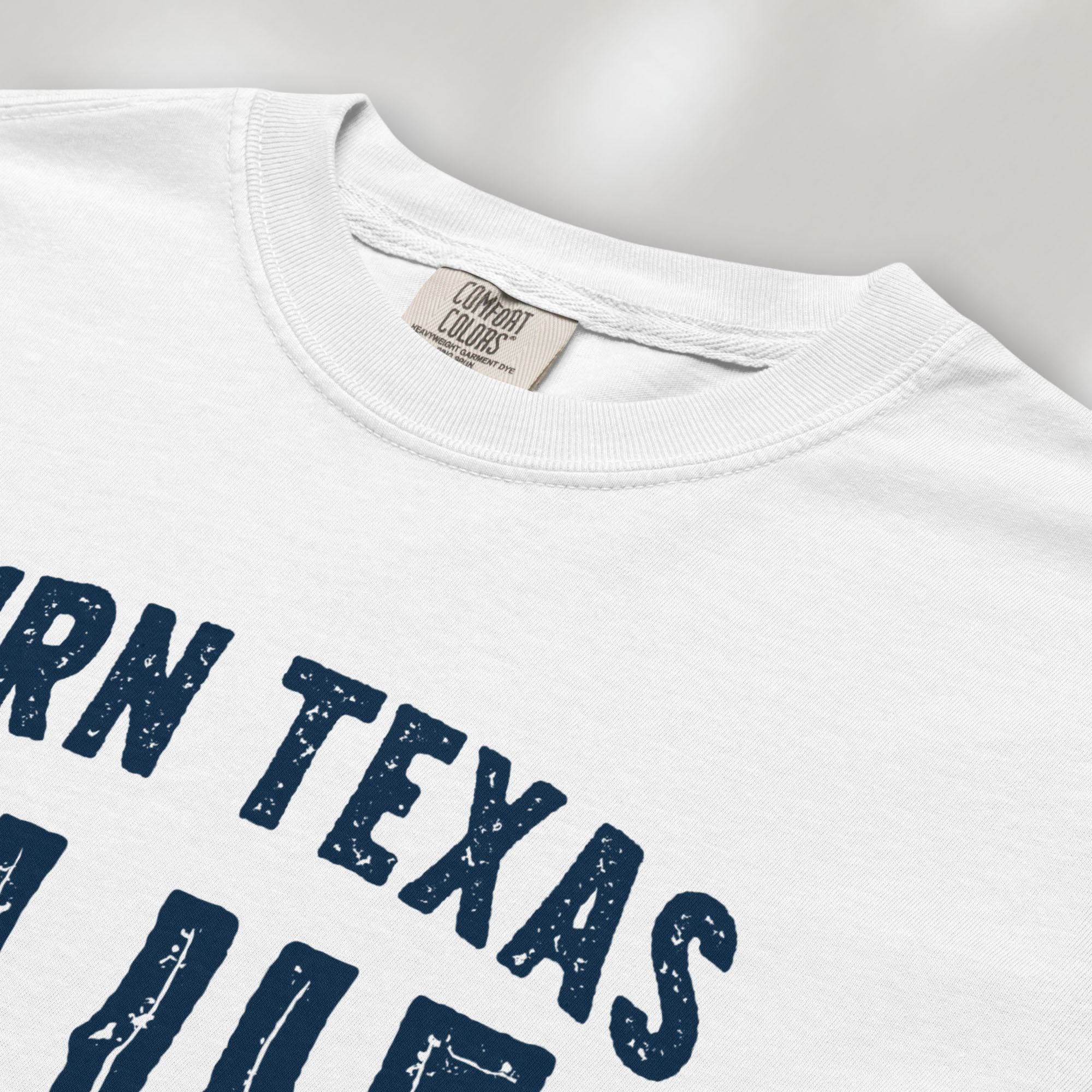 Closeup detail of white t-shirt featuring distressed "Turn Texas Blue" text with a small Texas icon and the phrase "Show Up Be Heard."