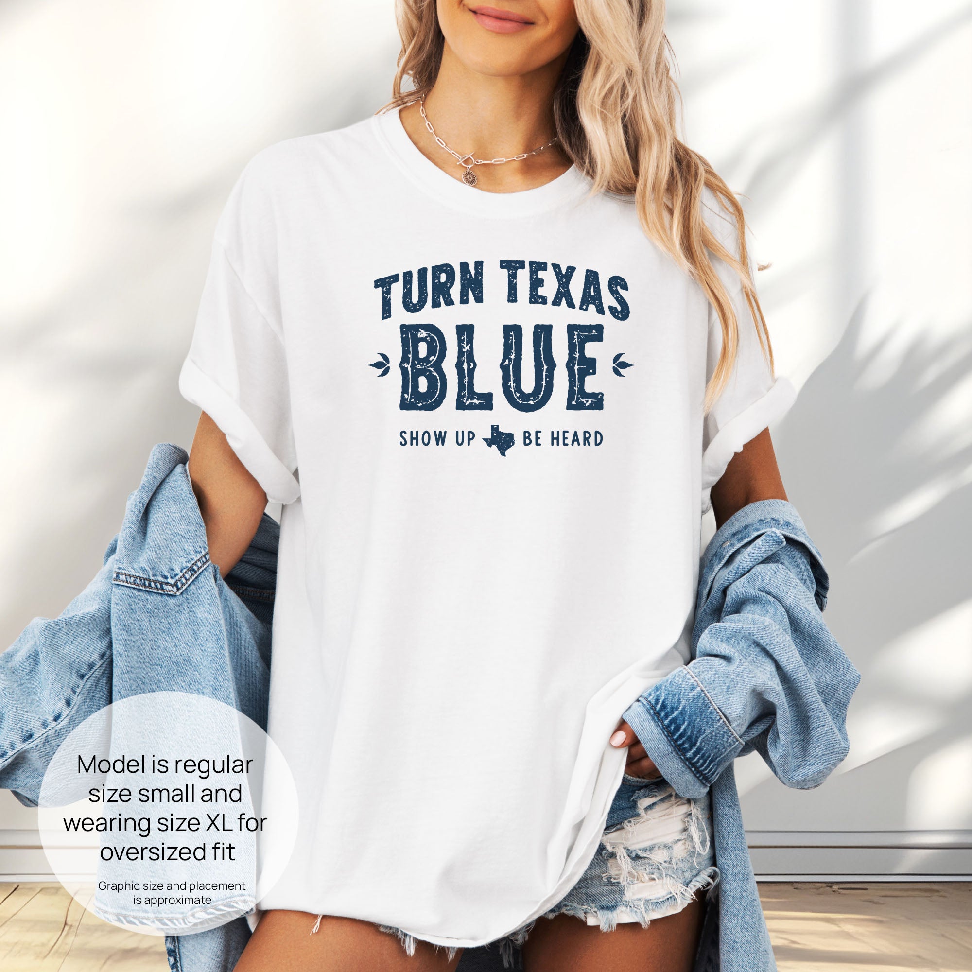 Female model wearing oversized white t-shirt featuring distressed "Turn Texas Blue" text with a small Texas icon and the phrase "Show Up Be Heard." Includes size and fit information for the model who is regular size small, and wearing a size XL shirt for an oversized fit.

