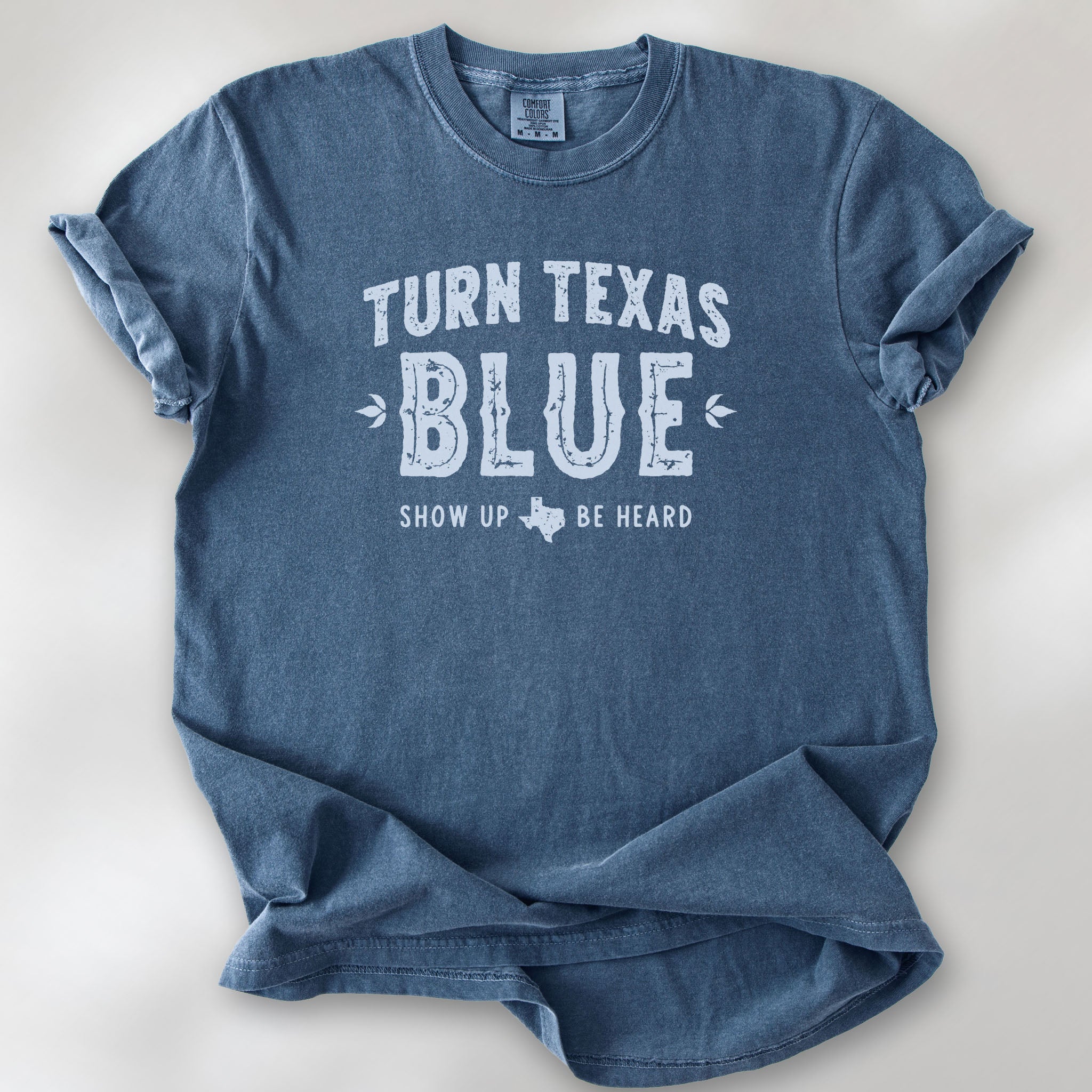 Denim t-shirt featuring distressed "Turn Texas Blue" text with a small Texas icon and the phrase "Show Up Be Heard."
