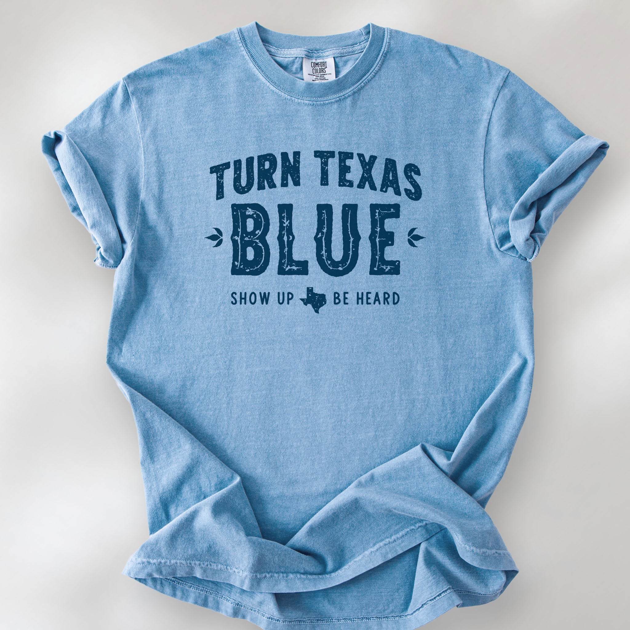 Washed denim t-shirt featuring distressed "Turn Texas Blue" text with a small Texas icon and the phrase "Show Up Be Heard."