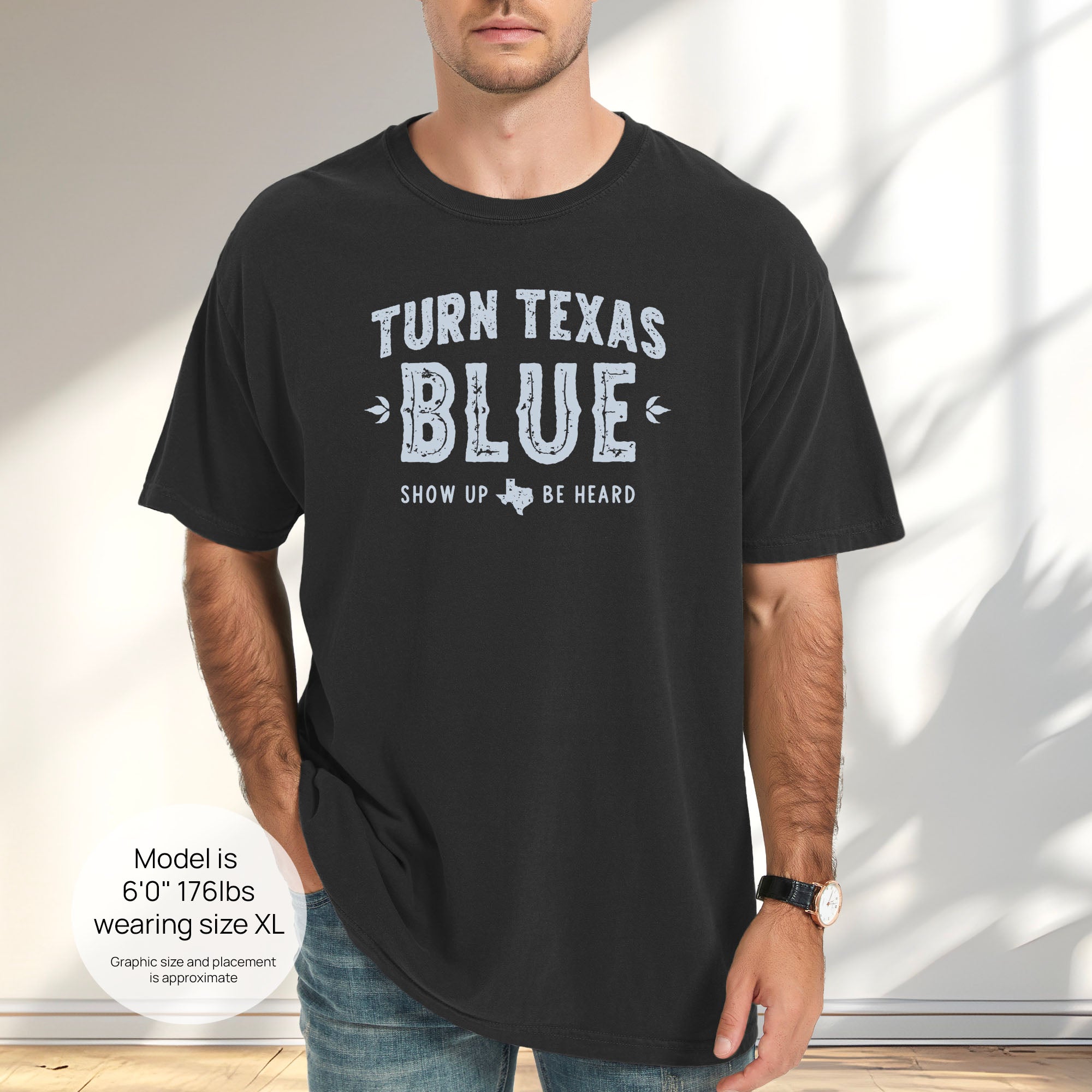 Male model wearing black t-shirt featuring distressed "Turn Texas Blue" text with a small Texas icon and the phrase "Show Up Be Heard." Includes size and fit information for the model who is 6 feet 0 inches, 176 pounds, and wearing a size XL shirt.
