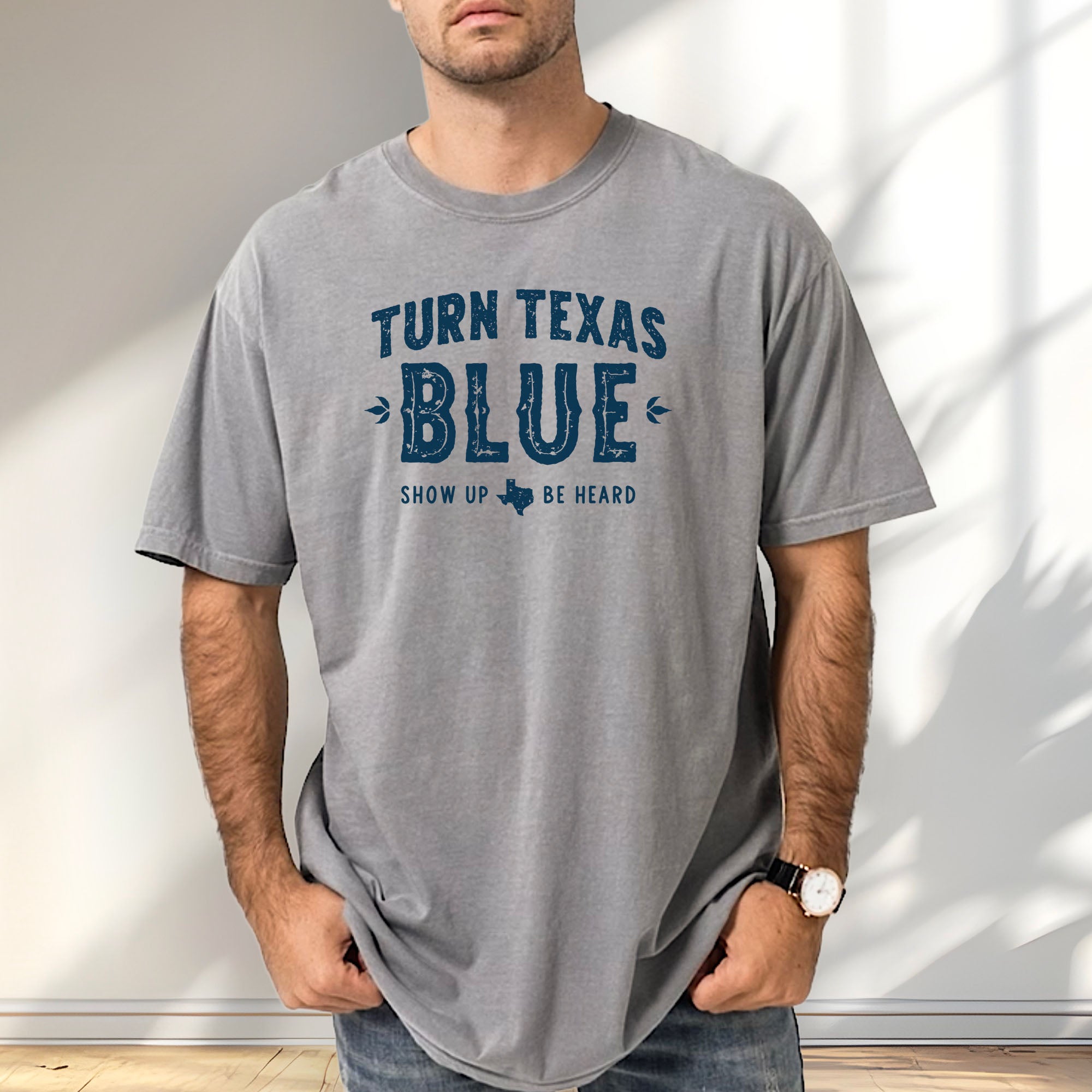 Male model wearing grey t-shirt featuring distressed "Turn Texas Blue" text with a small Texas icon and the phrase "Show Up Be Heard."