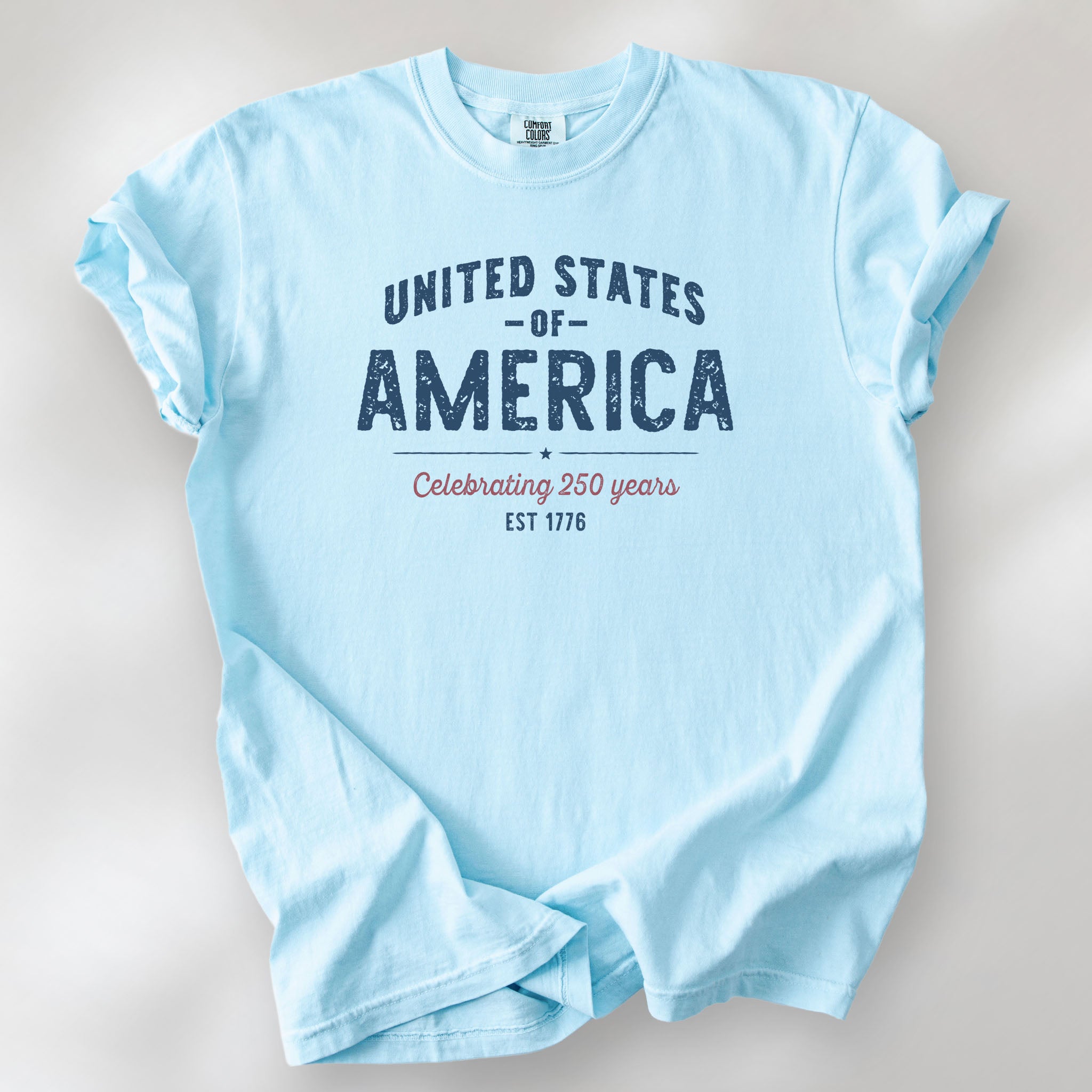 Chambray t-shirt with vintage style text reading “United States of America — Celebrating 250 Years — Est 1776”. 