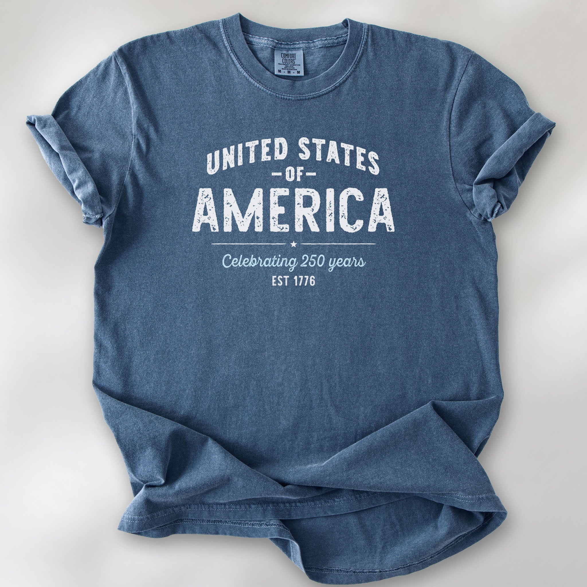 Denim t-shirt with vintage style text reading “United States of America — Celebrating 250 Years — Est 1776”. 