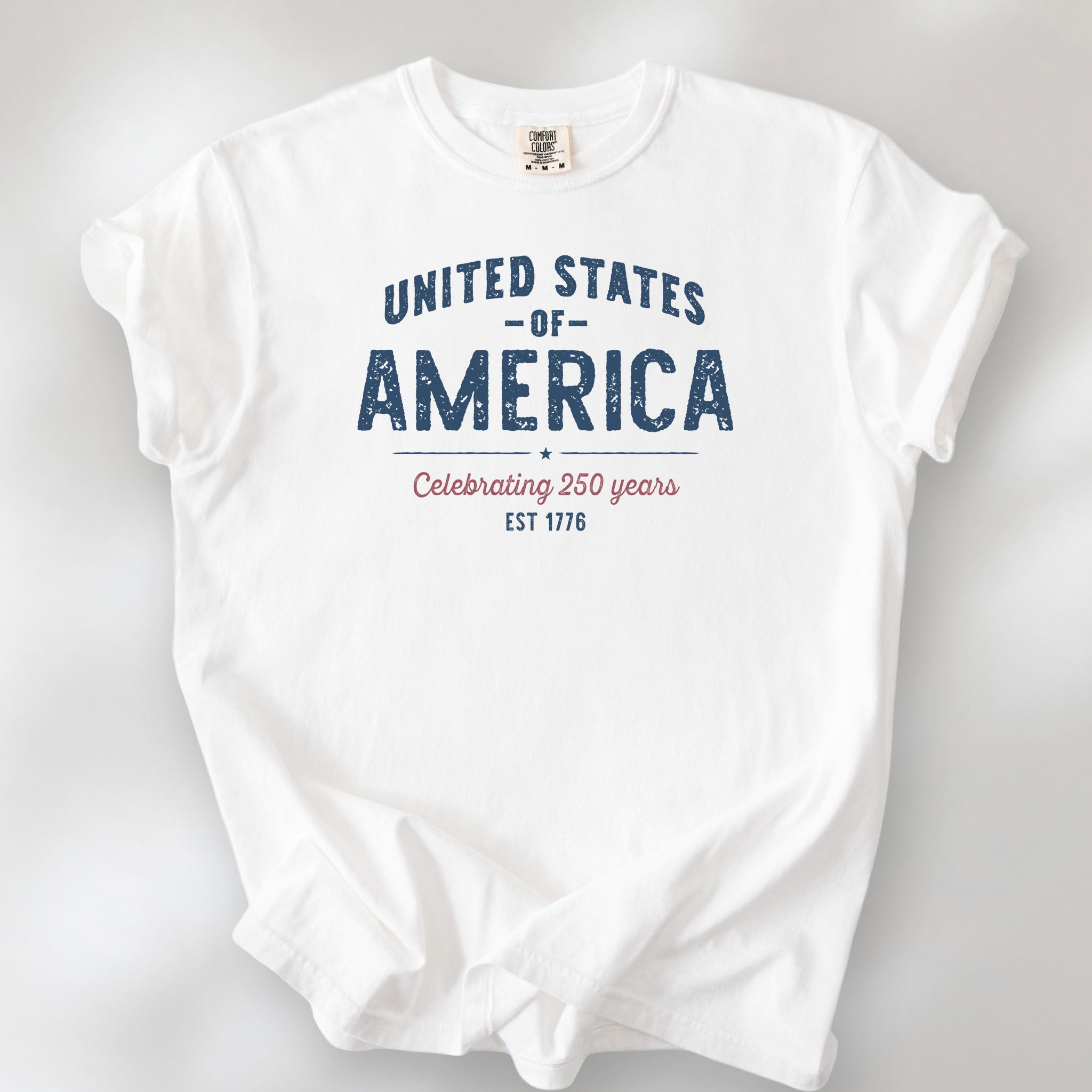 White t-shirt with vintage style text reading “United States of America — Celebrating 250 Years — Est 1776”. 