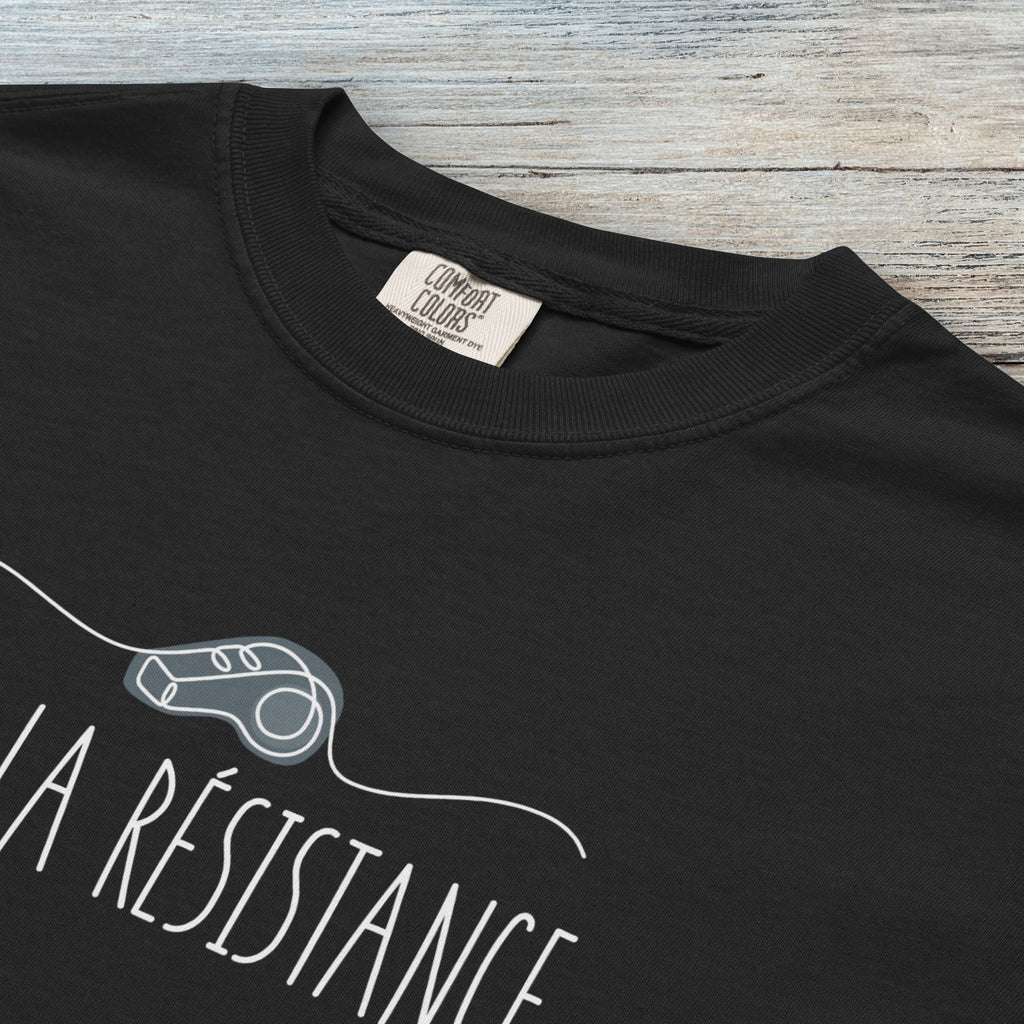 Closeup detail of black unisex t-shirt reading “Vive La Resistance” with a whistle illustration referencing community alert systems used to warn neighbors of ICE presence.