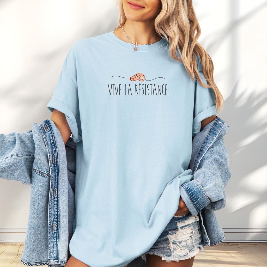 Female model wearing oversized chambray blue unisex t-shirt reading “Viva La Resistance” with a whistle illustration referencing community alert systems used to warn neighbors of ICE presence.