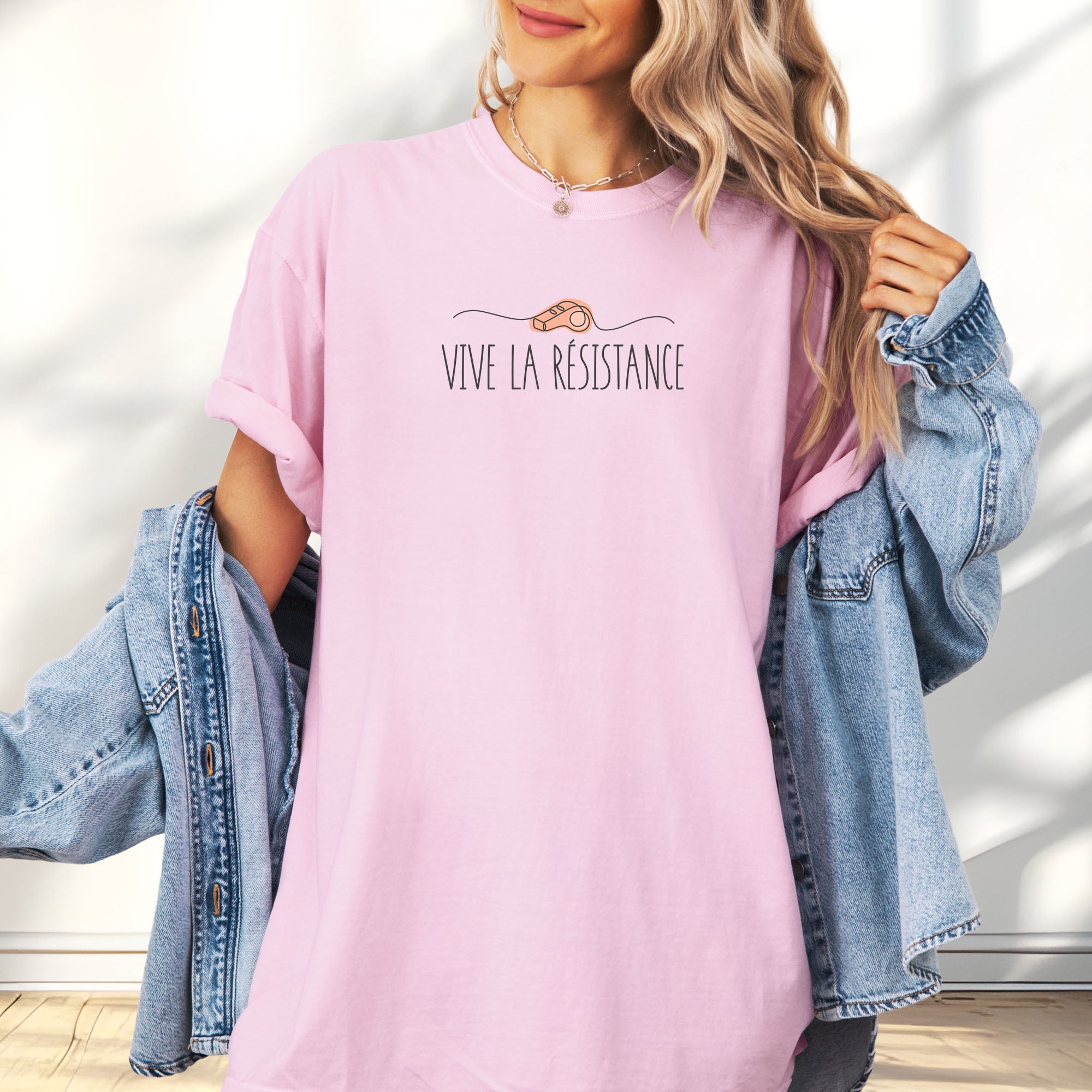 Female model wearing blossom unisex t-shirt reading “Viva La Resistance” with a whistle illustration referencing community alert systems used to warn neighbors of ICE presence.