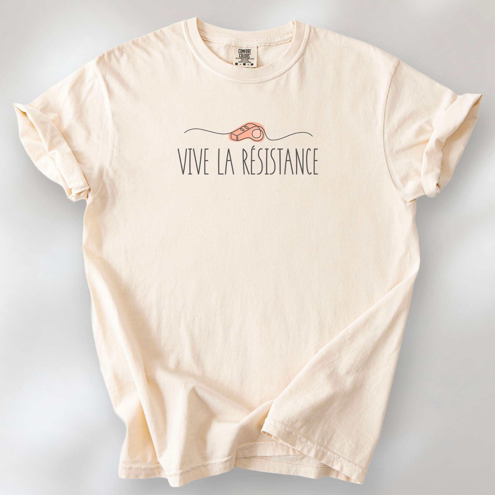 Ivory unisex t-shirt reading “Viva La Resistance” with a whistle illustration referencing community alert systems used to warn neighbors of ICE presence.