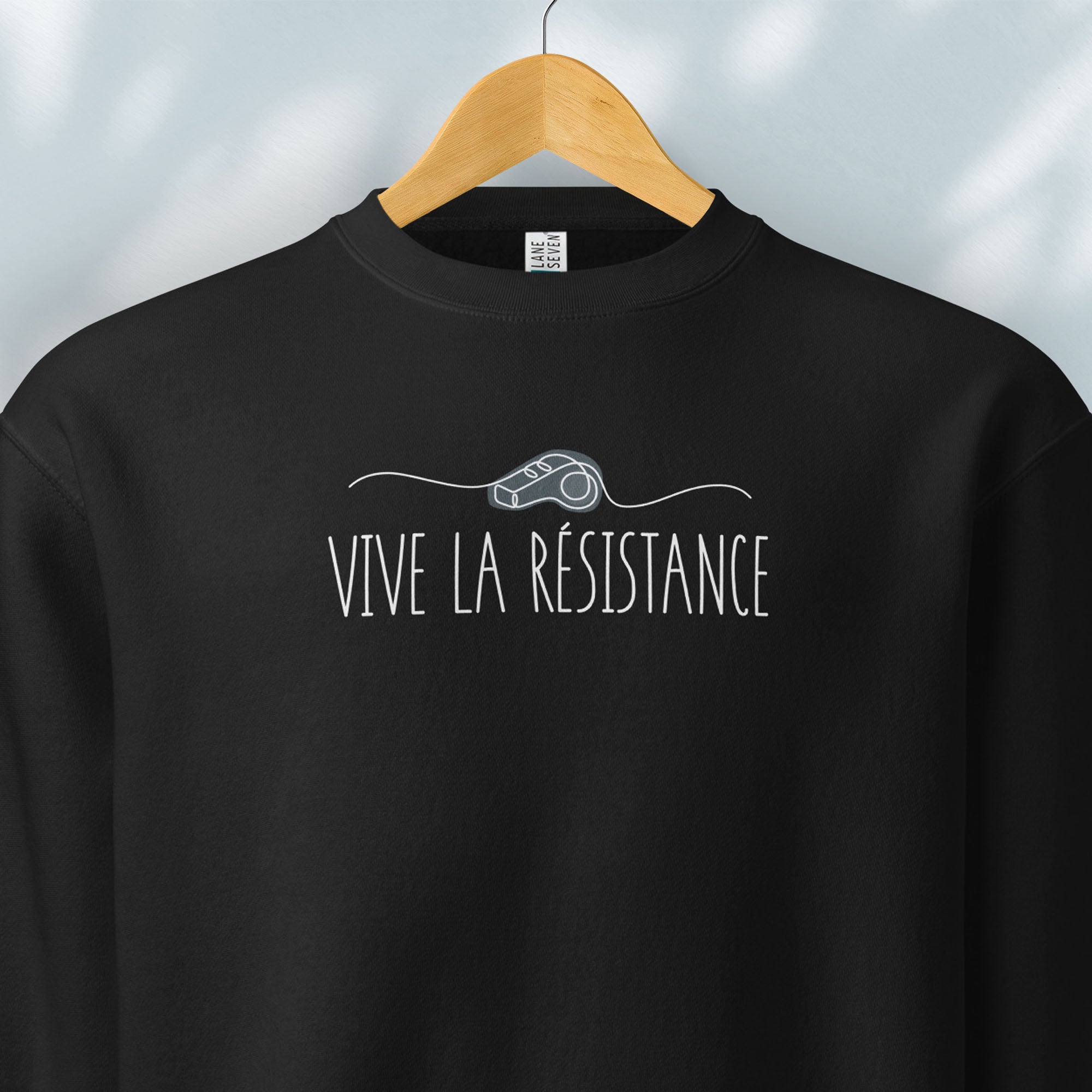 Hanging black sweatshirt reading “Viva La Resistance” with a whistle illustration referencing community alert systems used to warn neighbors of ICE presence.