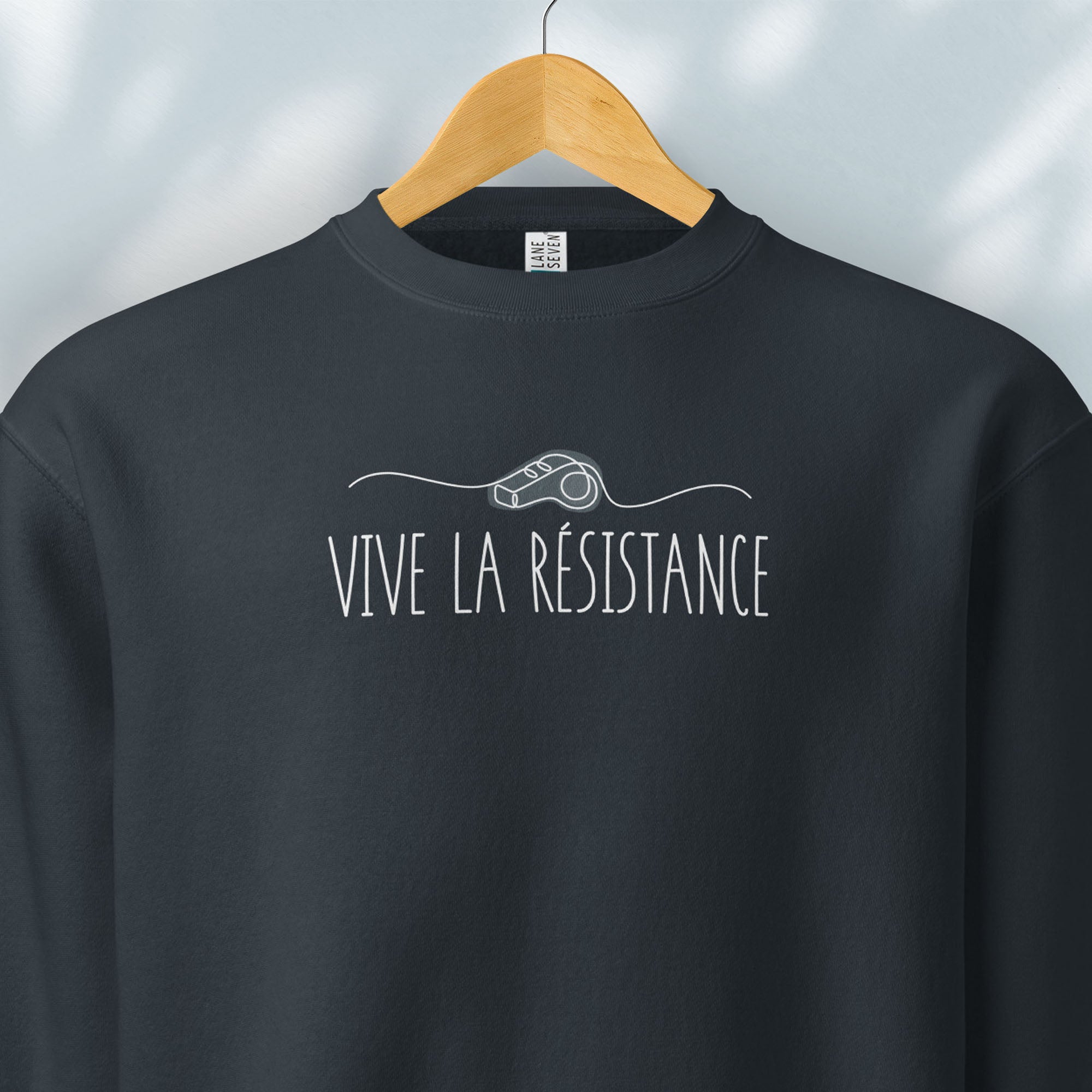 Hanging navy sweatshirt reading “Viva La Resistance” with a whistle illustration referencing community alert systems used to warn neighbors of ICE presence.