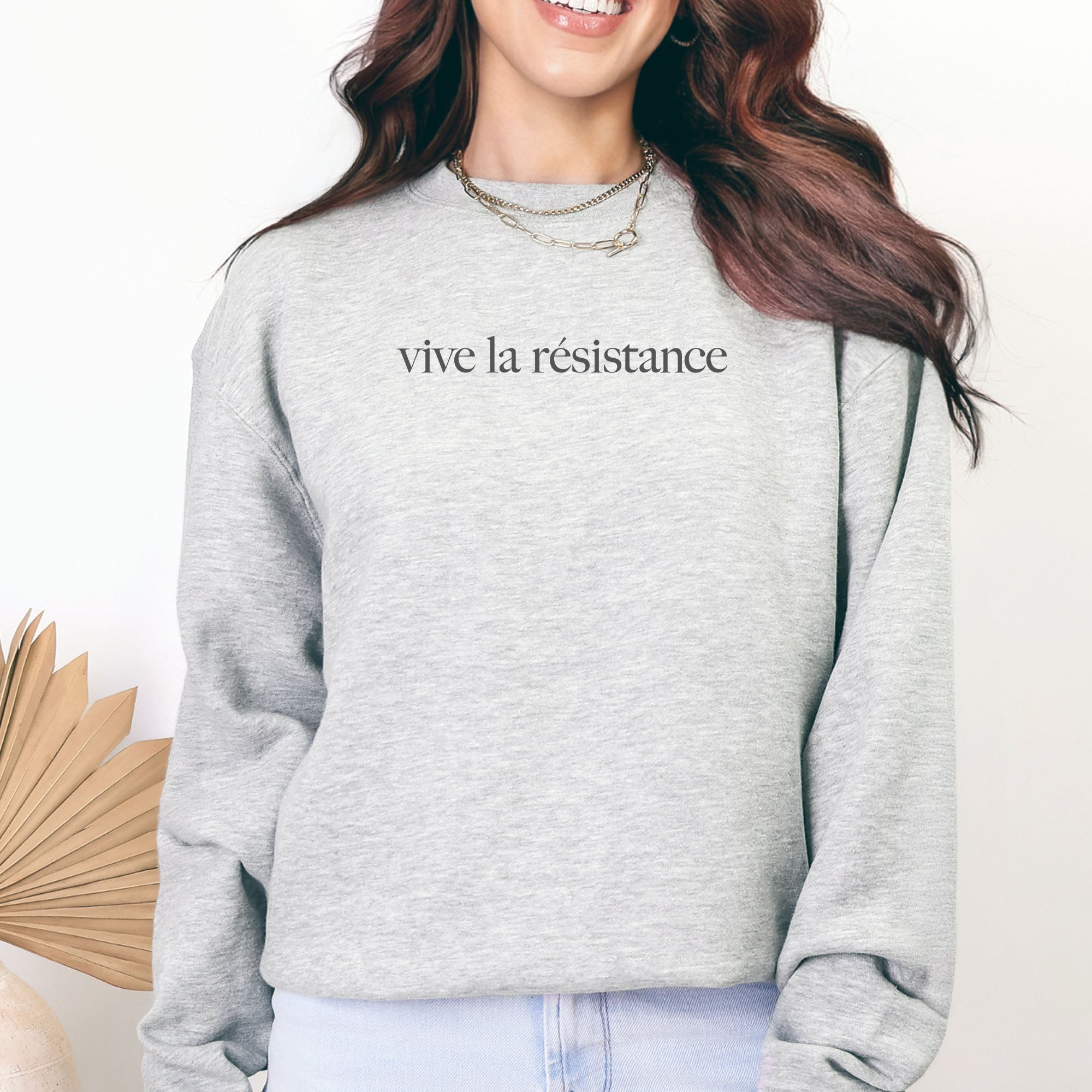 Female model wearing grey sweatshirt with minimalist serif text reading “vive la résistance.”