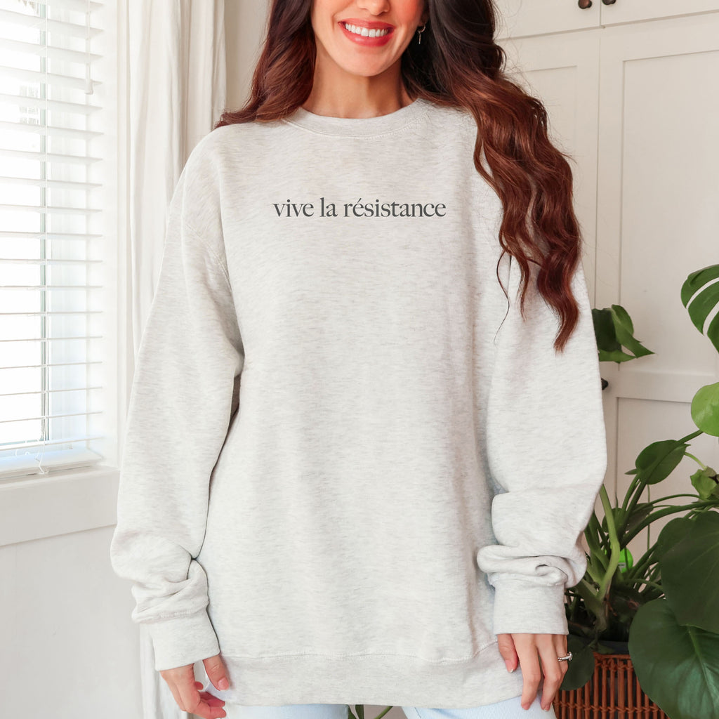 Female model wearing oatmeal sweatshirt with minimalist serif text reading “vive la résistance.”