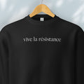 Hanging black sweatshirt with minimalist serif text reading “vive la résistance.”