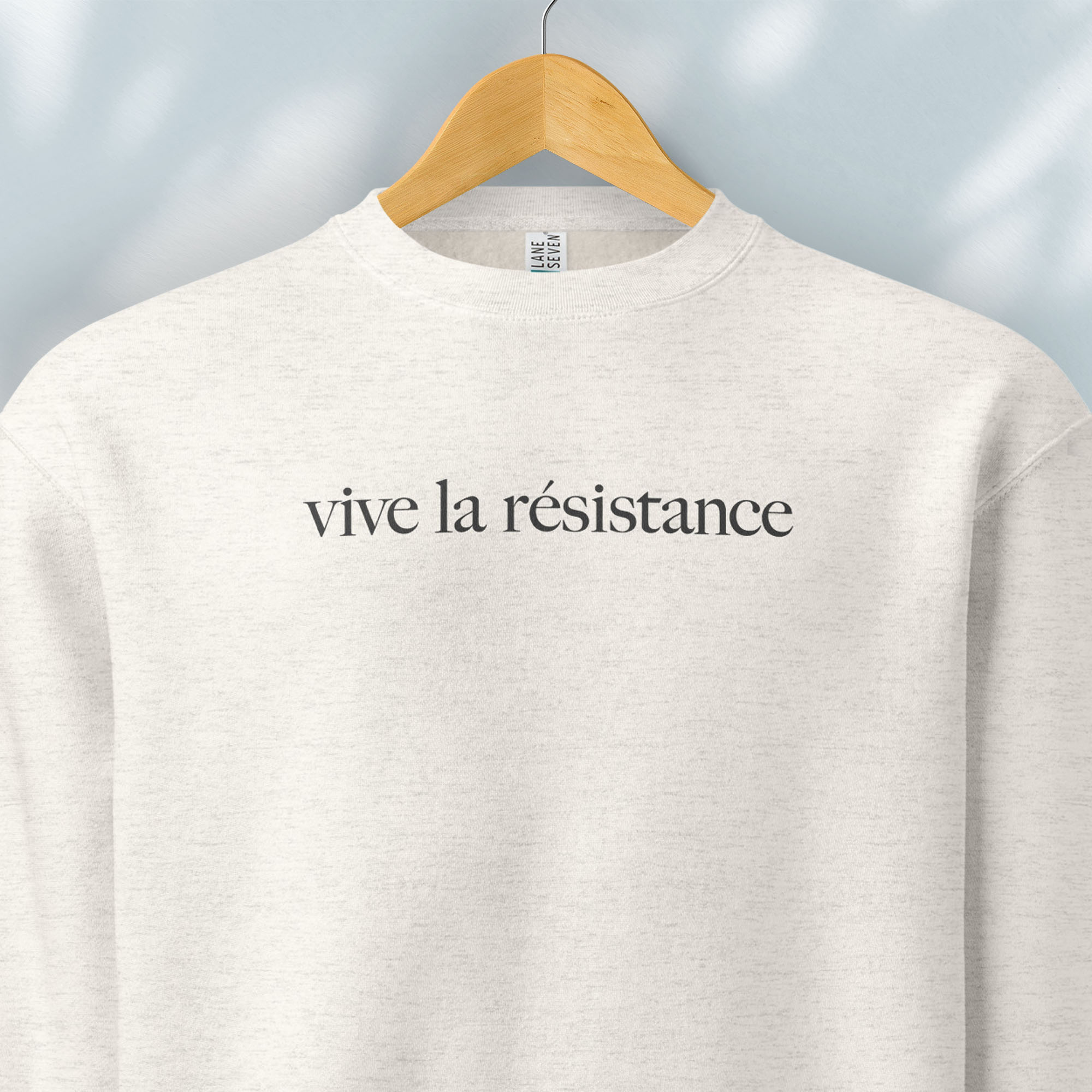 Hanging oatmeal sweatshirt with minimalist serif text reading “vive la résistance.”