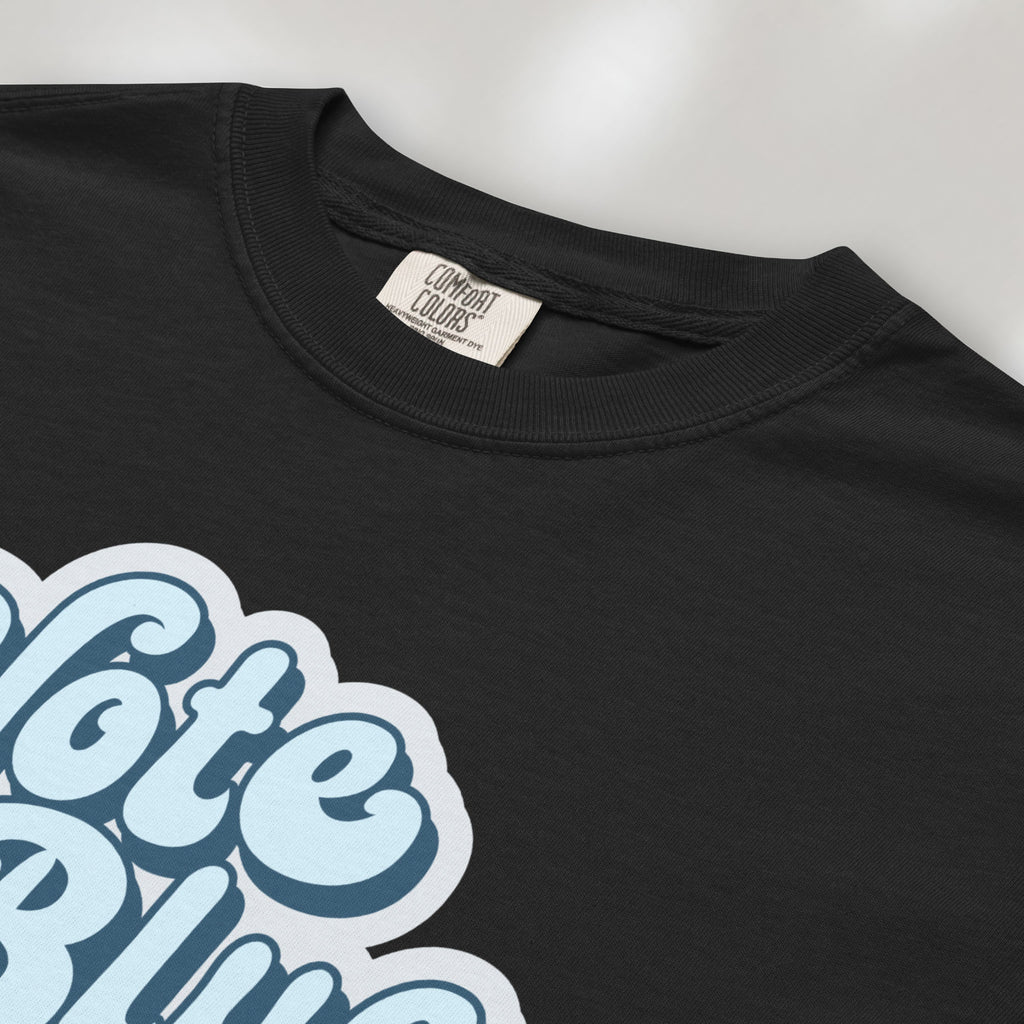 Closeup detail of black t-shirt featuring a retro blue "Vote Blue" script graphic.