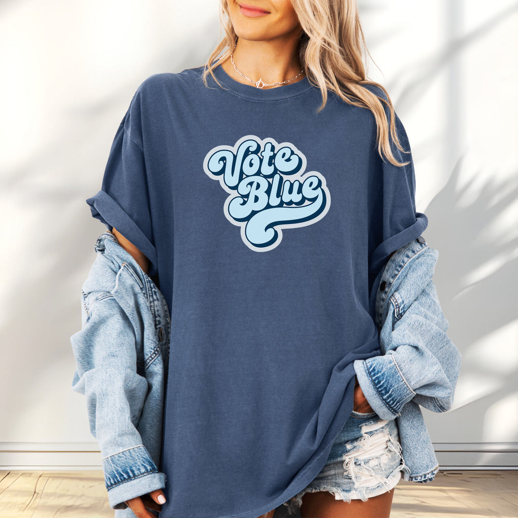 Female model wearing oversized denim t-shirt featuring a retro blue "Vote Blue" script graphic.