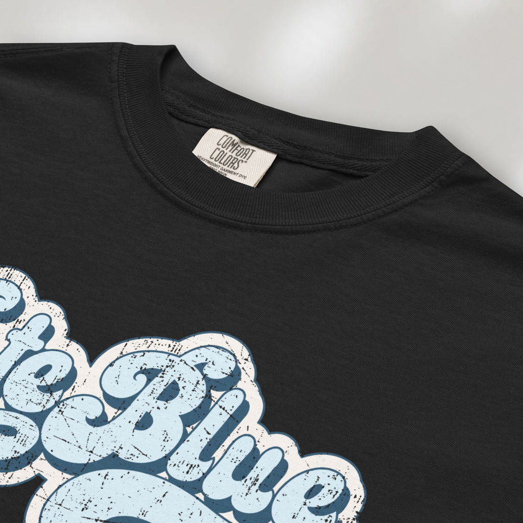 Closeup detail of black t-shirt featuring distressed retro script text reading "Vote Blue" in light blue vintage lettering.