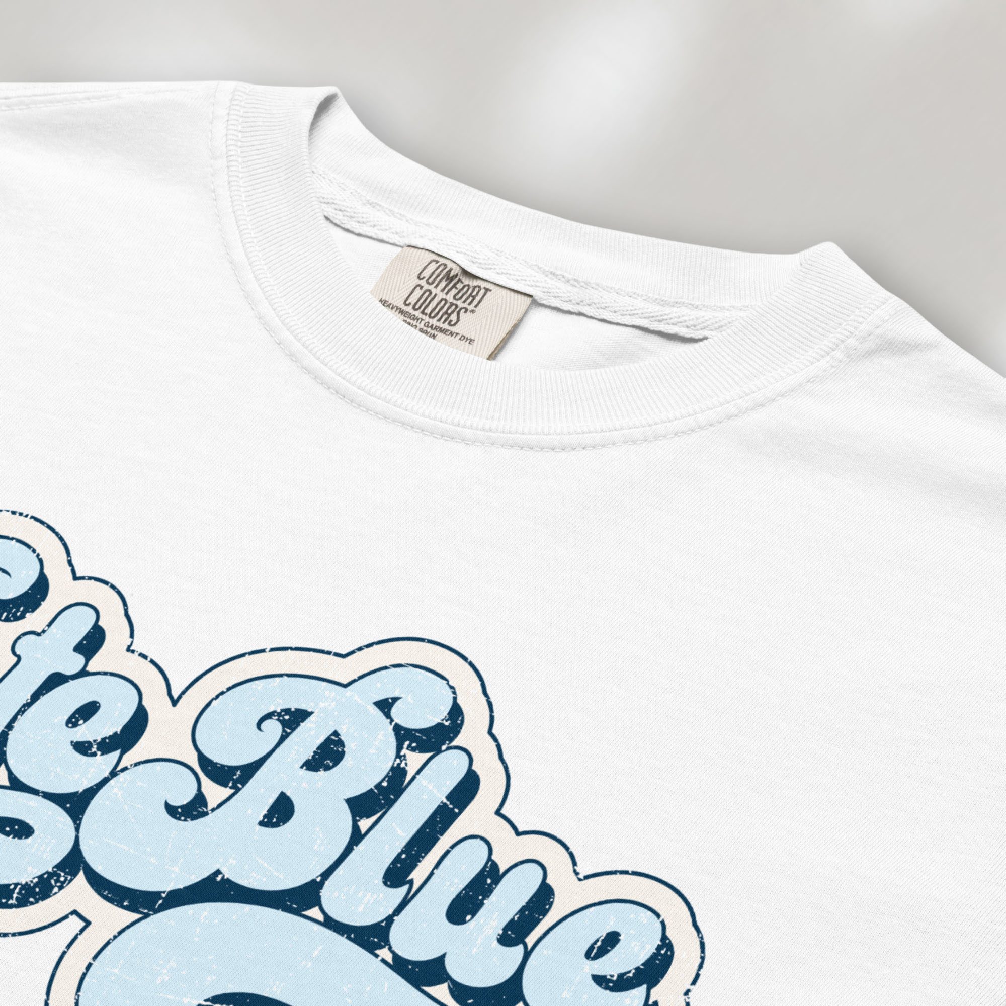 Closeup detail of white t-shirt featuring distressed retro script text reading "Vote Blue" in light blue vintage lettering.