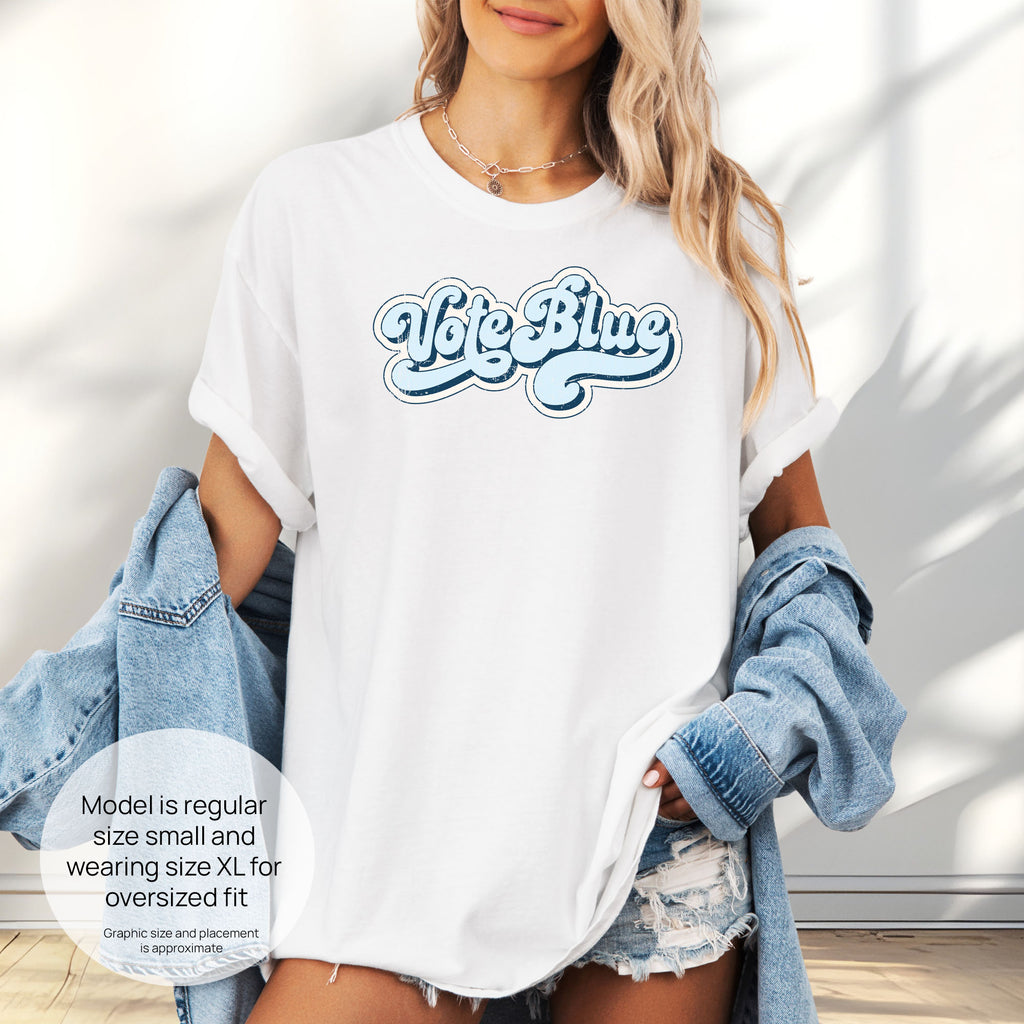 Female model wearing oversized white t-shirt featuring distressed retro script text reading "Vote Blue" in light blue vintage lettering. Includes size and fit information for the model who is regular size small, and wearing a size XL shirt for an oversized fit.
