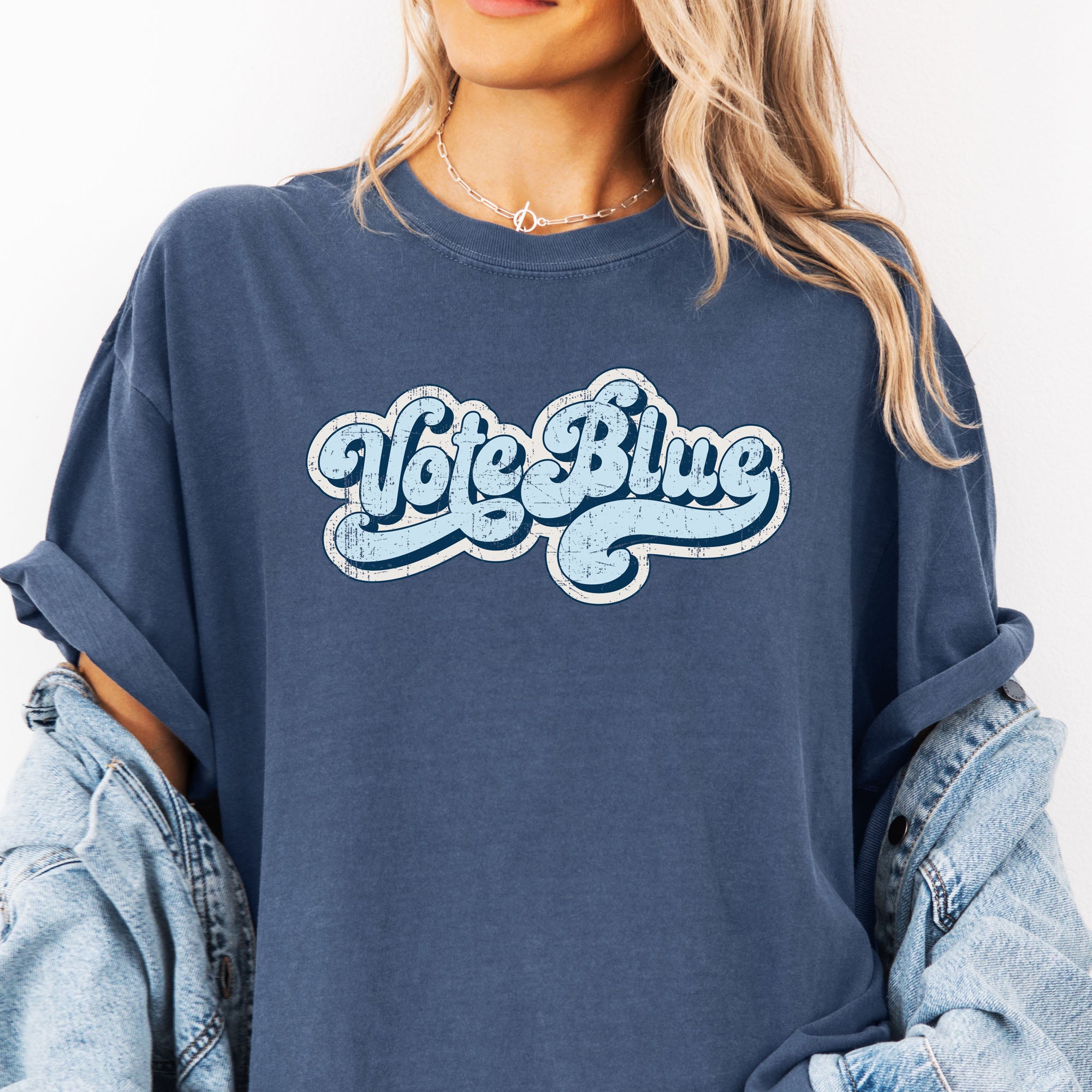 Female model wearing denim t-shirt featuring distressed retro script text reading "Vote Blue" in light blue vintage lettering.