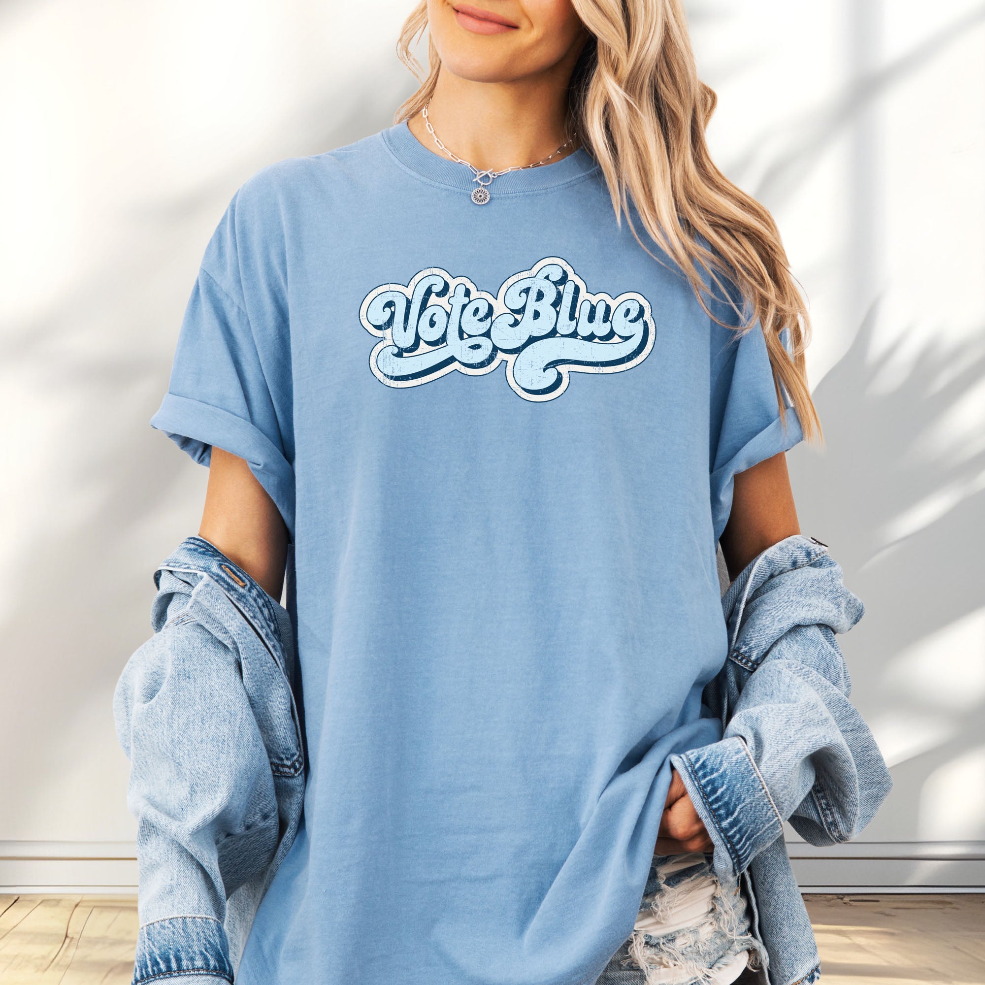Female model wearing oversized washed denim t-shirt featuring distressed retro script text reading "Vote Blue" in light blue vintage lettering.