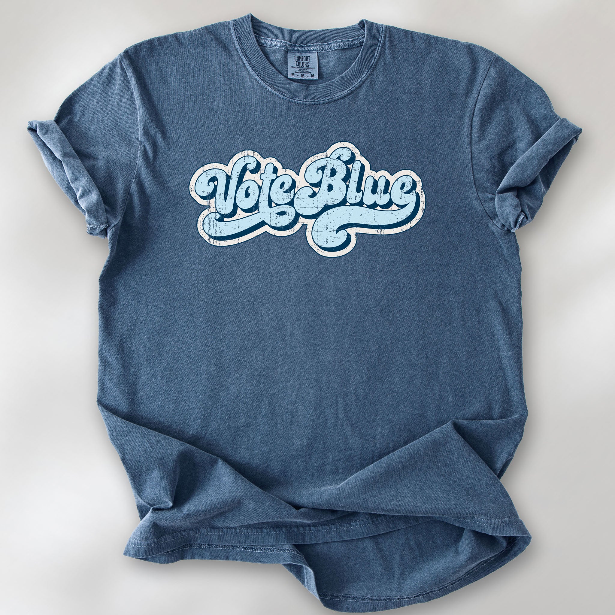 Denim t-shirt featuring distressed retro script text reading "Vote Blue" in light blue vintage lettering.