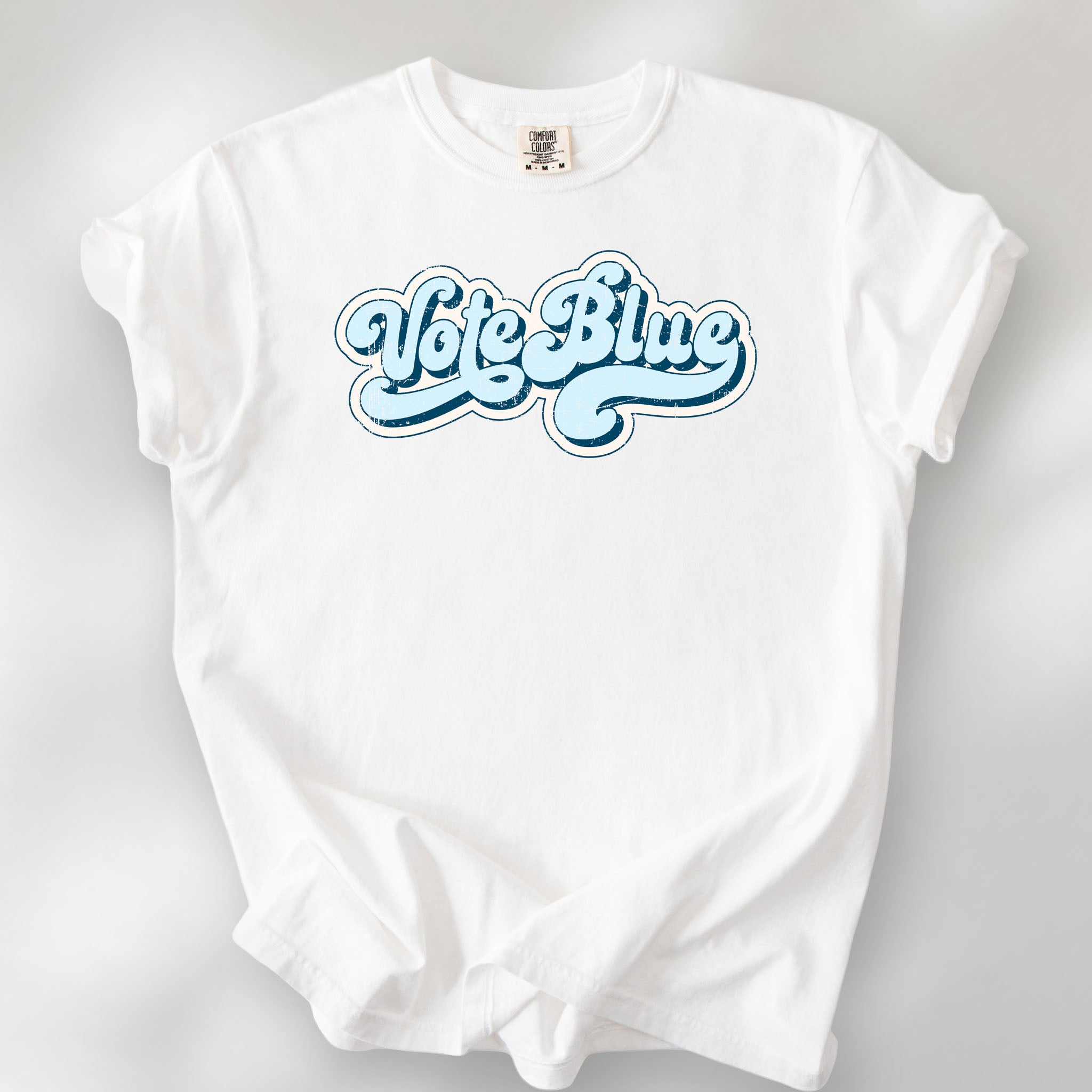 White t-shirt featuring distressed retro script text reading "Vote Blue" in light blue vintage lettering.