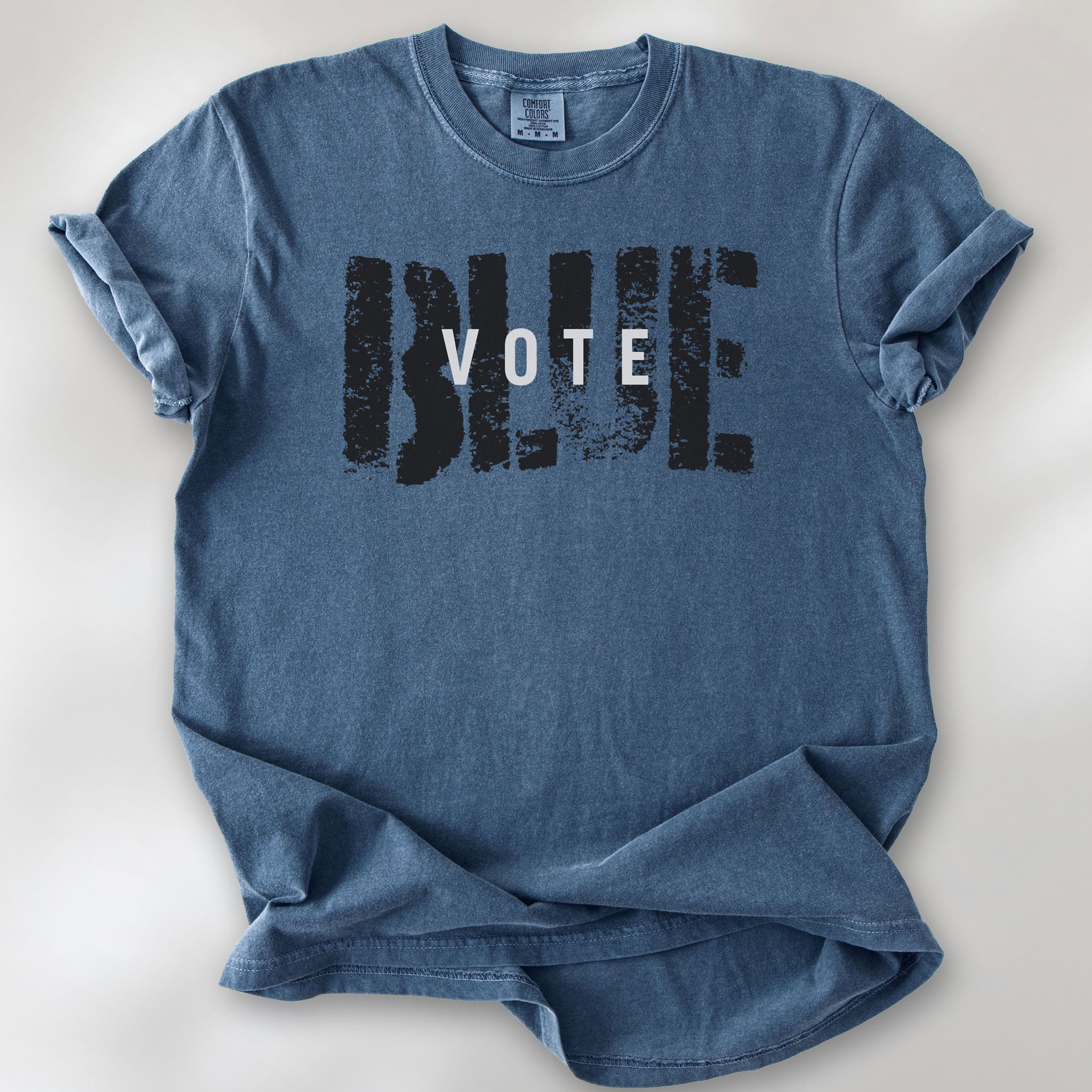 Denim t-shirt with the word "vote" atop the word "blue" in a grunge background texture.