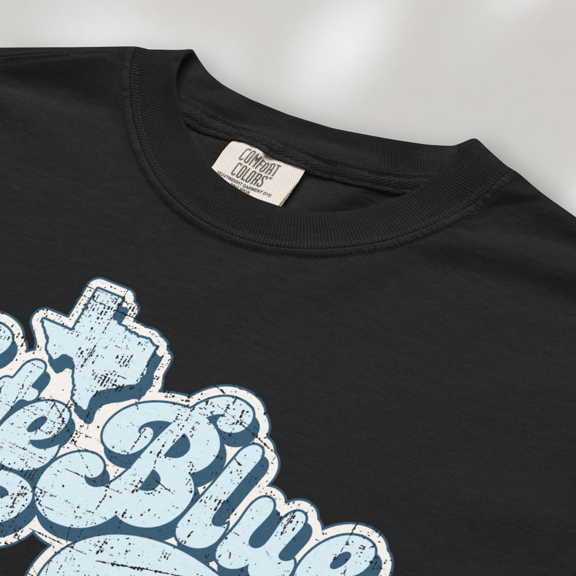 Closeup detail of black t-shirt featuring distressed retro "Vote Blue" script lettering with the outline of Texas above the design.