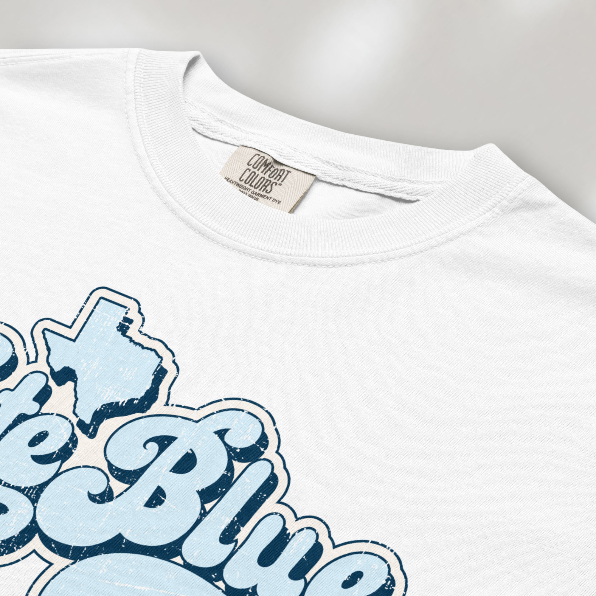 Closeup detail of white t-shirt featuring distressed retro "Vote Blue" script lettering with the outline of Texas above the design.