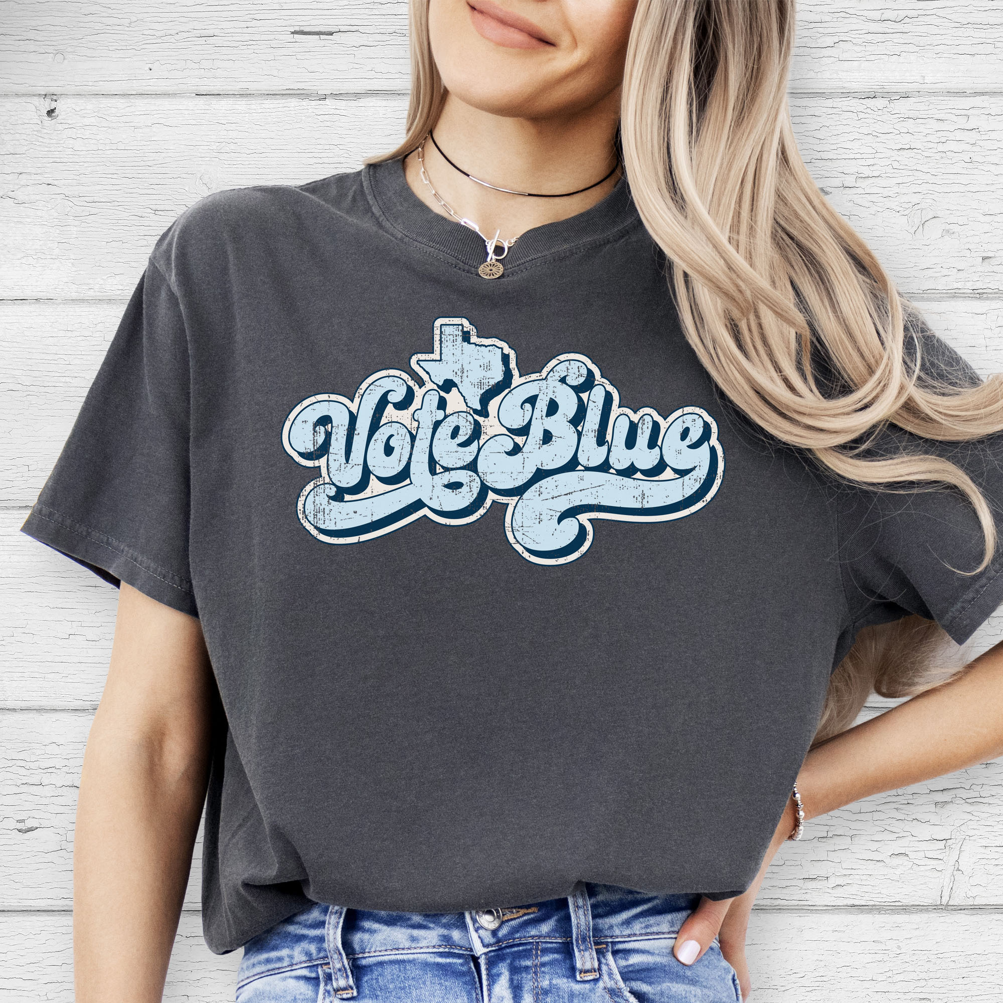 Female model wearing pepper t-shirt featuring distressed retro "Vote Blue" script lettering with the outline of Texas above the design.