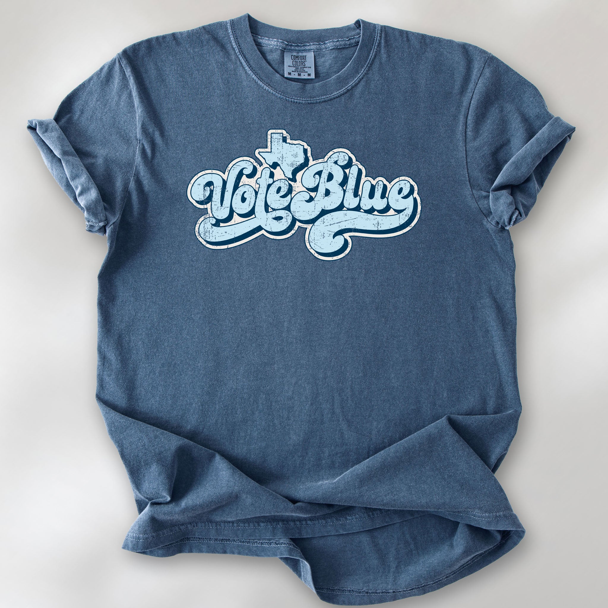 Denim t-shirt featuring distressed retro "Vote Blue" script lettering with the outline of Texas above the design.