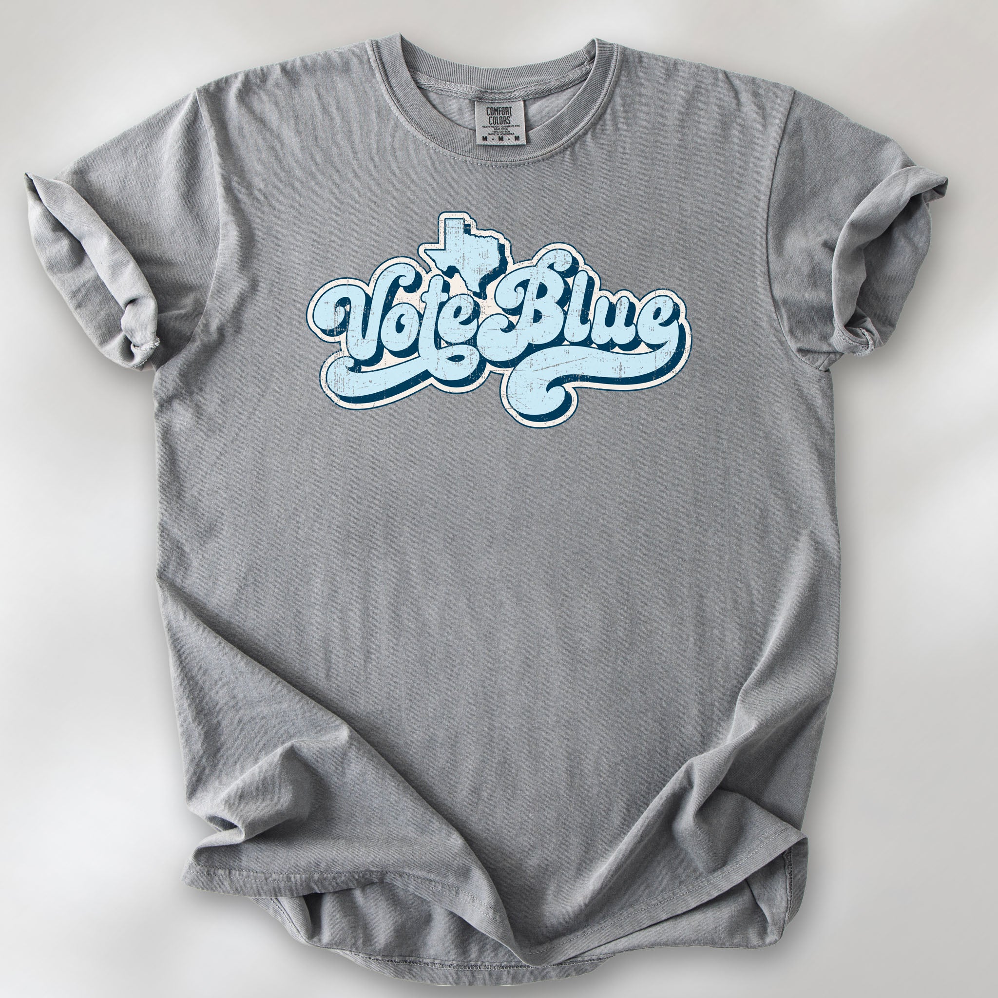 Grey t-shirt featuring distressed retro "Vote Blue" script lettering with the outline of Texas above the design.