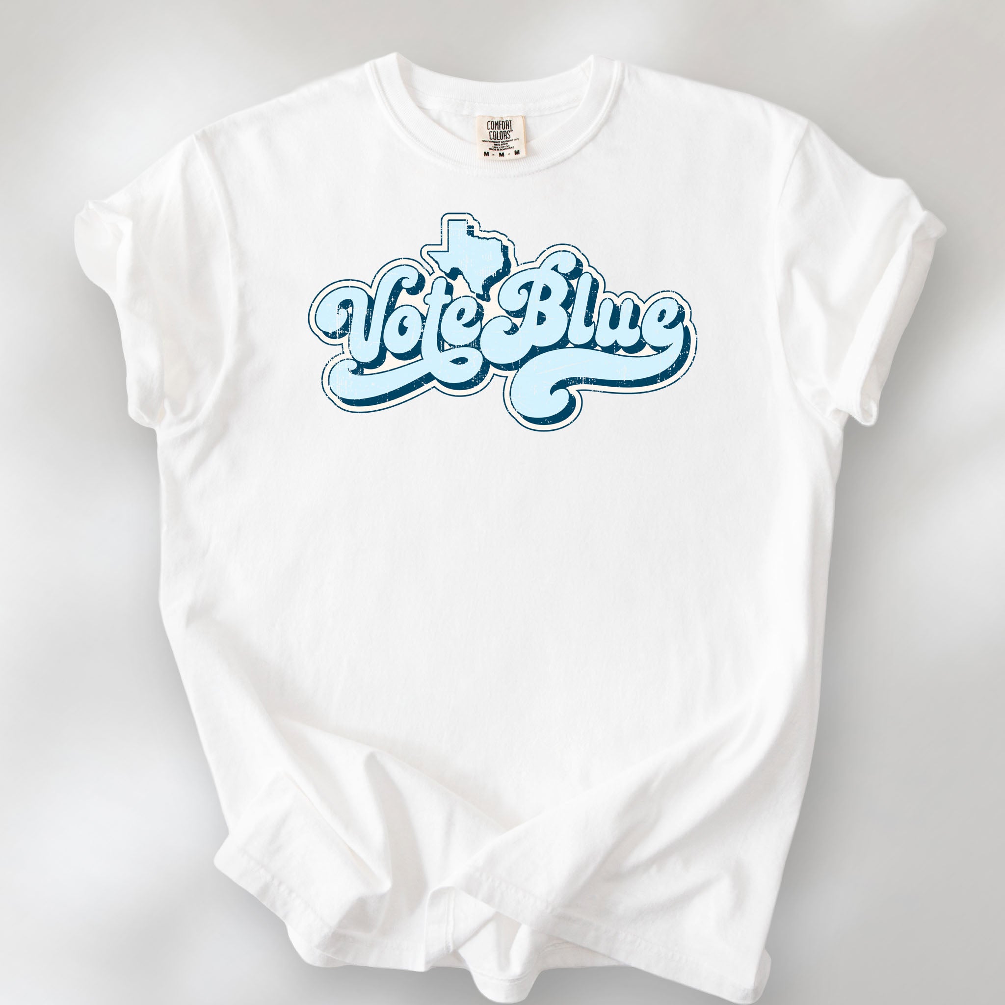 White t-shirt featuring distressed retro "Vote Blue" script lettering with the outline of Texas above the design.