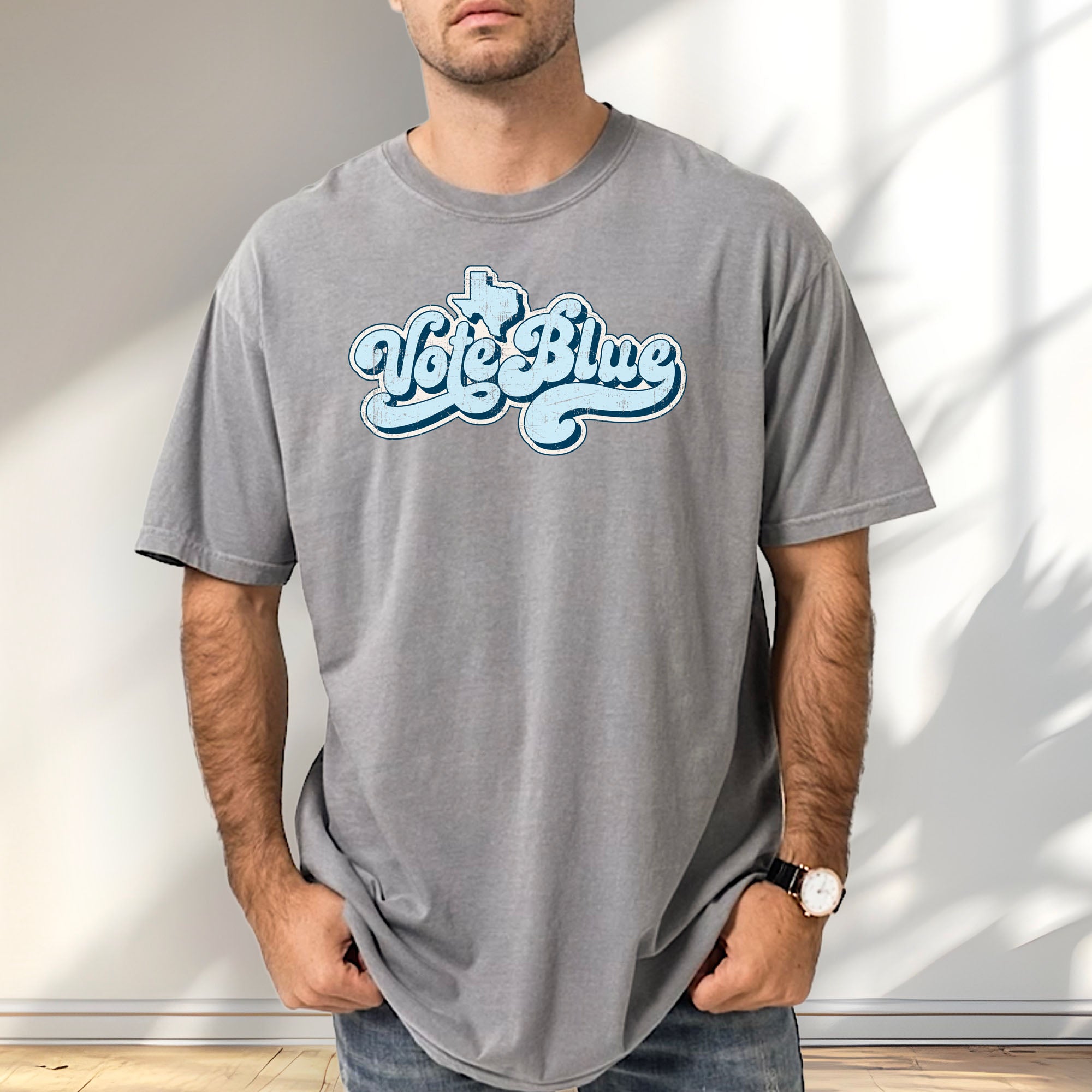 Male model wearing grey t-shirt featuring distressed retro "Vote Blue" script lettering with the outline of Texas above the design.