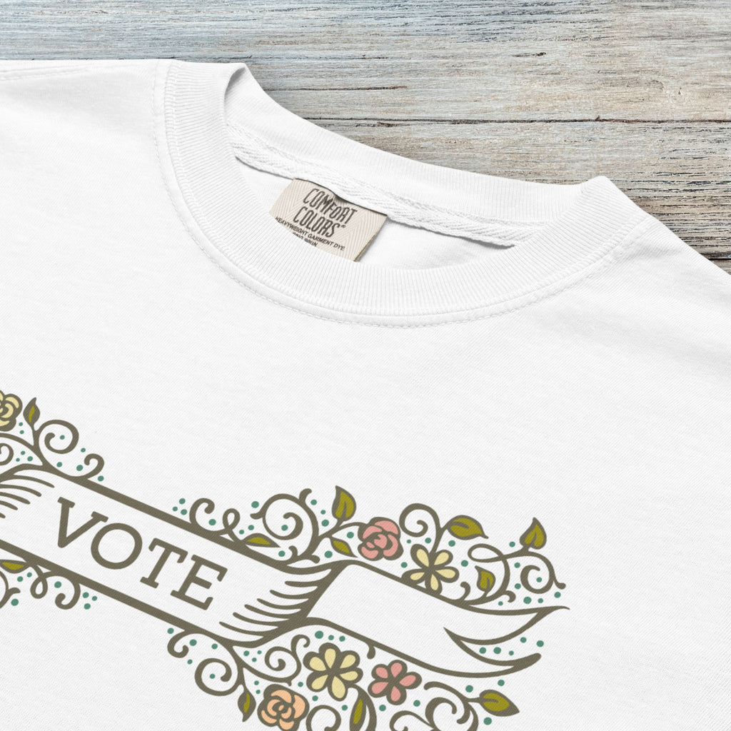 Closeup detail of white t-shirt with vintage style floral illustration and a banner reading “vote” in the center.
